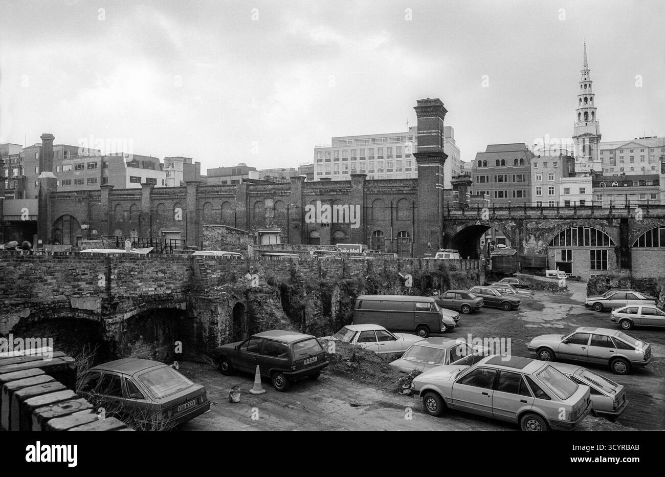 Schwarzweiß-Archivfoto von London aus dem Jahr 1986 mit Blick westlich zur St. Brides Kirche an der Fleet Street, über einem offenen Parkplatz auf unebenem Gelände. Das Gebiet wurde seitdem umfassend umgebaut, aber es wird angenommen, dass es sich um einen Parkplatz auf einer Bombenanlage aus dem Zweiten Weltkrieg auf beiden Seiten der Pilgrim Street handelt, der durch die Eisenbahnbögen in der Mittelweite zu sehen ist. Stockfoto