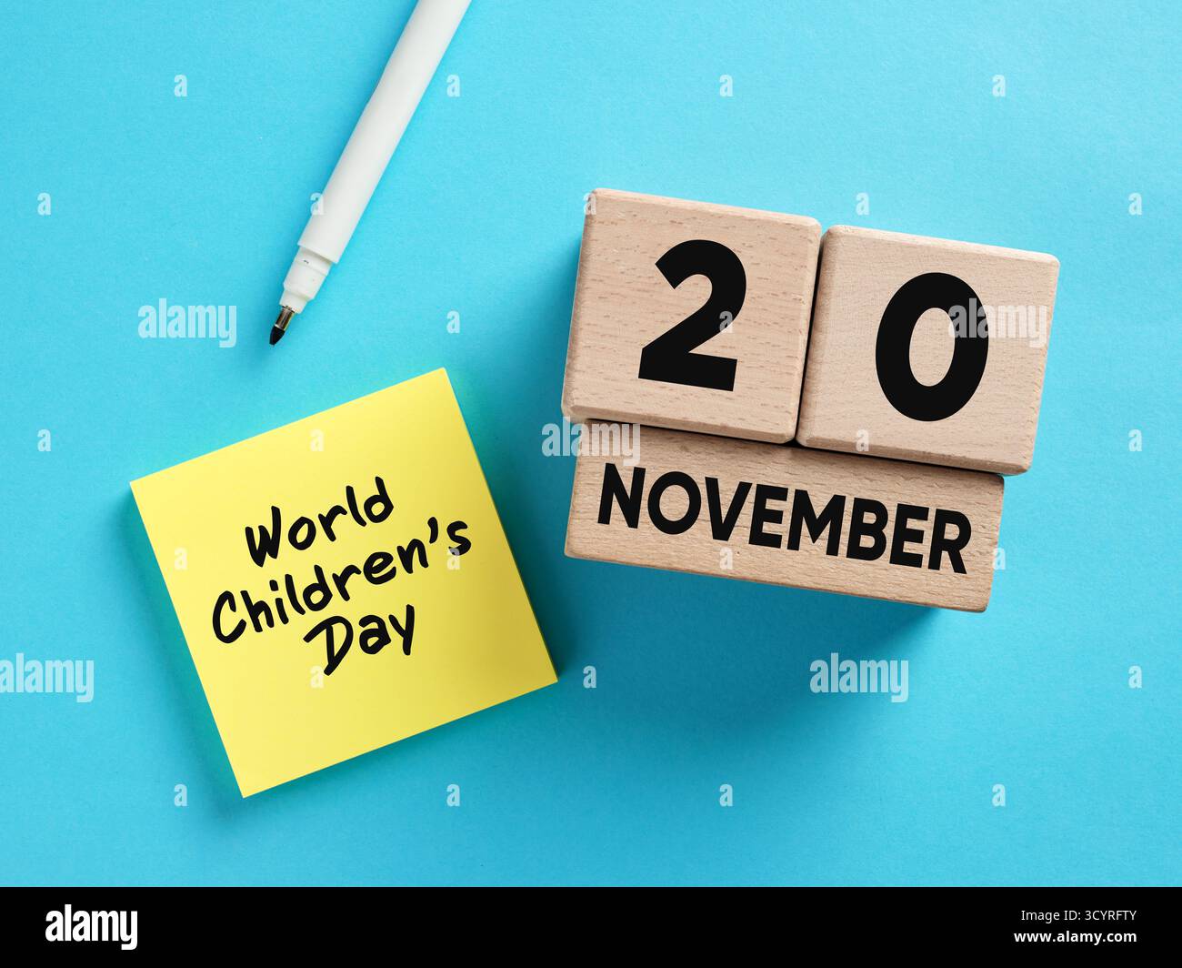 Holzkalender mit dem 20. November, dem Weltkindertag, begleitet von einer gelben Haftnotiz und einem weißen Markierstift auf blauem Hintergrund Stockfoto