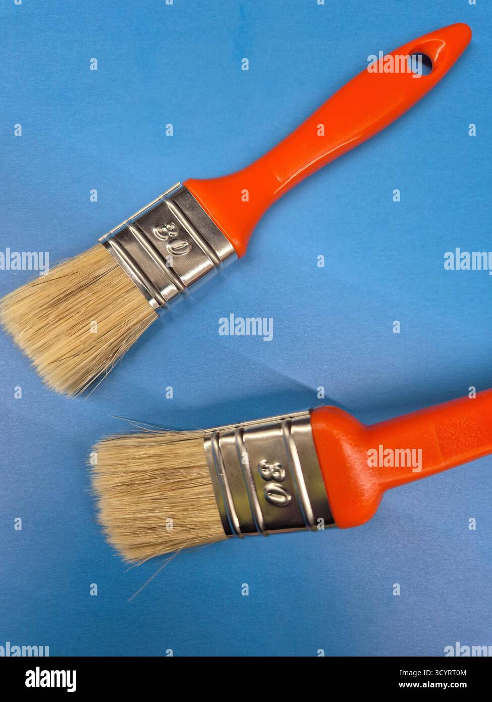 Zwei Pinsel mit leuchtend orangefarbenen Griffen, einsatzbereit für Reparaturen oder Kunstwerke auf blauem Hintergrund - Smartphone-aufgenommenes Stockfoto