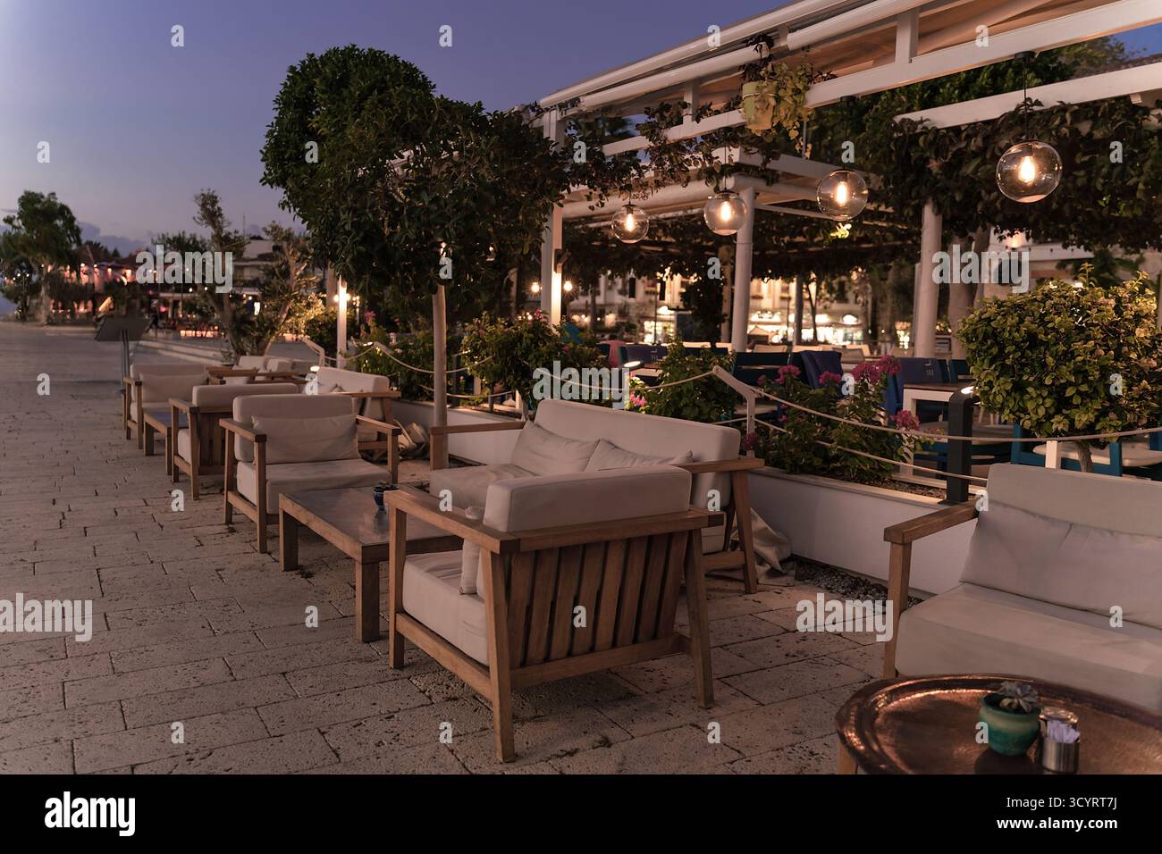 Sitzbereich im Freien mit Holzstühlen unter sanfter Beleuchtung, umgeben von üppigem Grün, schaffen eine gemütliche und einladende Atmosphäre Stockfoto