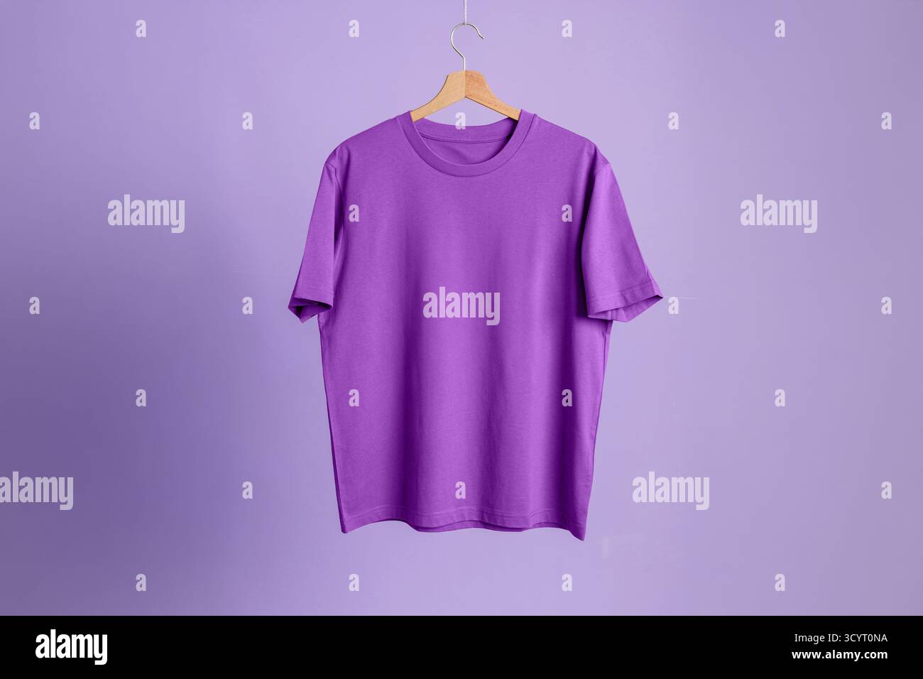 Lila Kurzarm-T-Shirt auf hölzernem Aufhänger, koordinierter Fliederhintergrund. Mockup-Vorlage für Kleidung. Minimalistische monochromatische Präsentation. Stockfoto