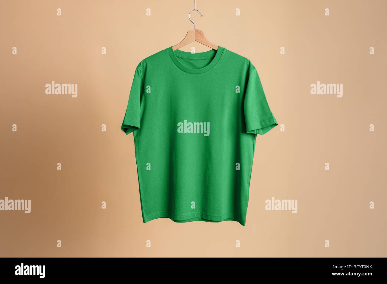 Hellgrünes Kurzarm-T-Shirt auf hölzernem Aufhänger, beigefarbener Hintergrund. Mockup-Vorlage für Freizeitkleidung. Saubere und minimalistische Präsentation. Stockfoto