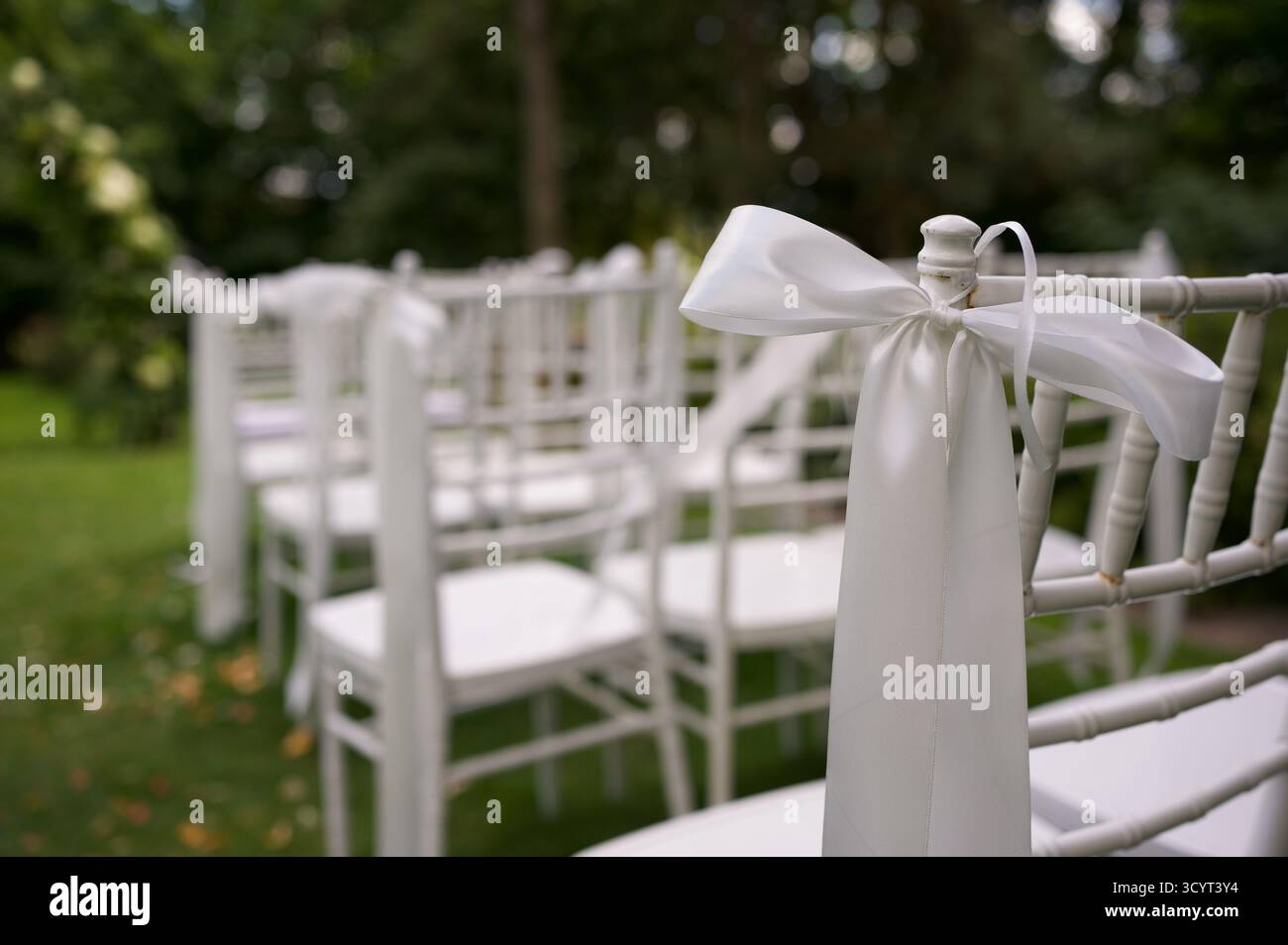 Weiße Stühle mit Bändern für eine Hochzeitszeremonie im Freien. Stockfoto