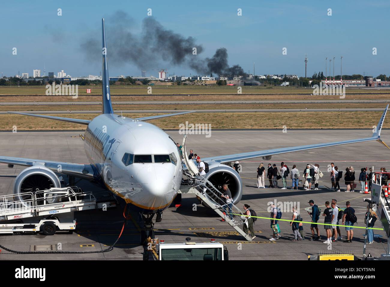 02.09.2024, Deutschland, Brandenburg, Schönefeld - Reisende steigen am Flughafen BER an Bord eines Ryanair-Flugzeugs. Im Hintergrund eine Feuerübung durch den Flughafenfeuer b Stockfoto