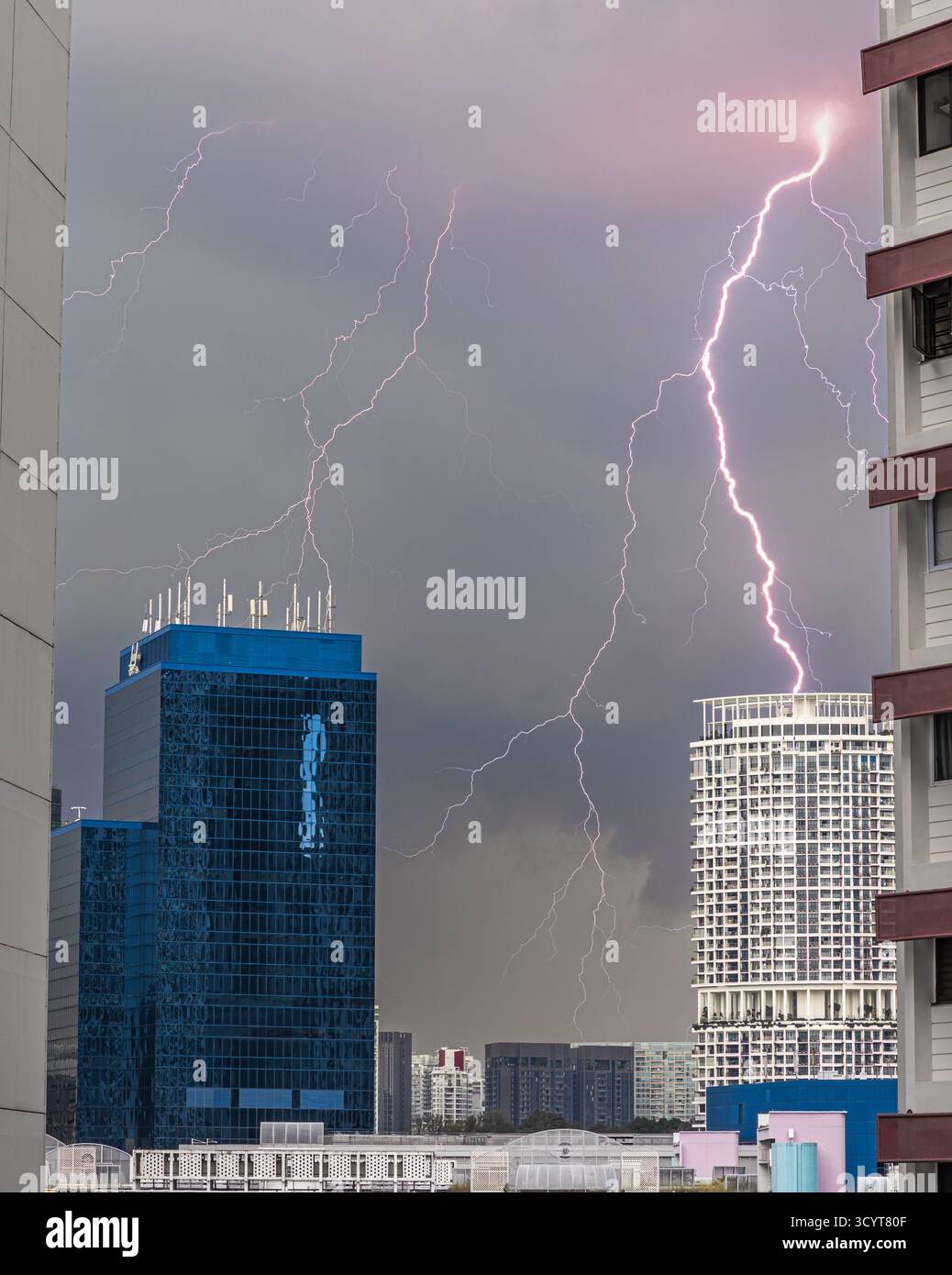Blitze treffen in der Nähe moderner Hochhäuser während eines Gewitters in Singapur, was die Kraft der Natur vor einer städtischen Skyline unterstreicht. Stockfoto