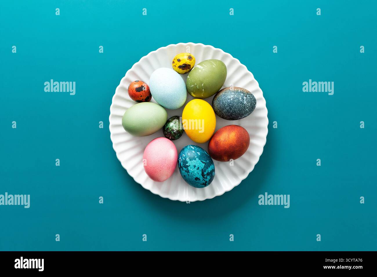 Festliche, farbenfrohe Eier in verschiedenen Farben sind ordentlich auf einem dekorativen Teller angeordnet und symbolisieren Ostertraditionen und Frühlingsfeste mit lebhaften Farben Stockfoto