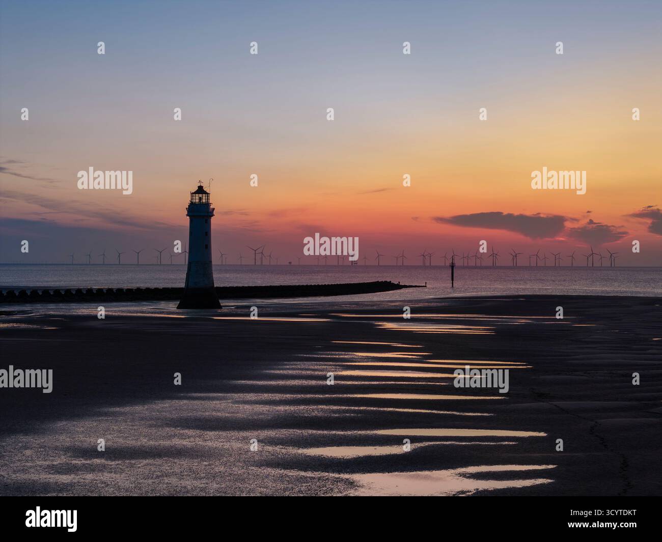 WIRRAL, MERSEYSIDE, ENGLAND - 16. AUGUST 2025: Barch Rock Lighthouse in der Abenddämmerung an der Küste in New Brighton, Wirral, England, mit Offshore-Windkraftanlage Stockfoto