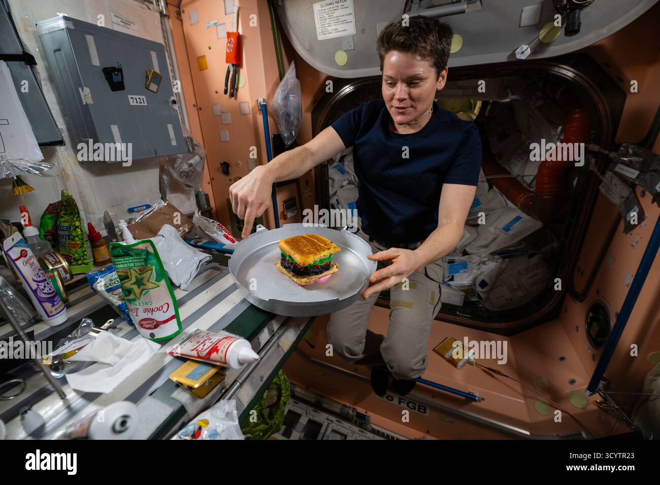ISS - 13. Juni 2025 - NASA-Astronaut und Expedition 73 Flight Engineer Anne McClain zeigt einen Hamburger-Kuchen, um 200 kumulative Weltraumtage für JAXA (Japan Aerospace Exploration Agency) Astronaut Takuya Onishi (außerhalb des Rahmens) seit seinem ersten Raumflug als Expedition 48-49 Flight Engineer im Jahr 2016 zu feiern - Foto: Geopix/NASA Stockfoto