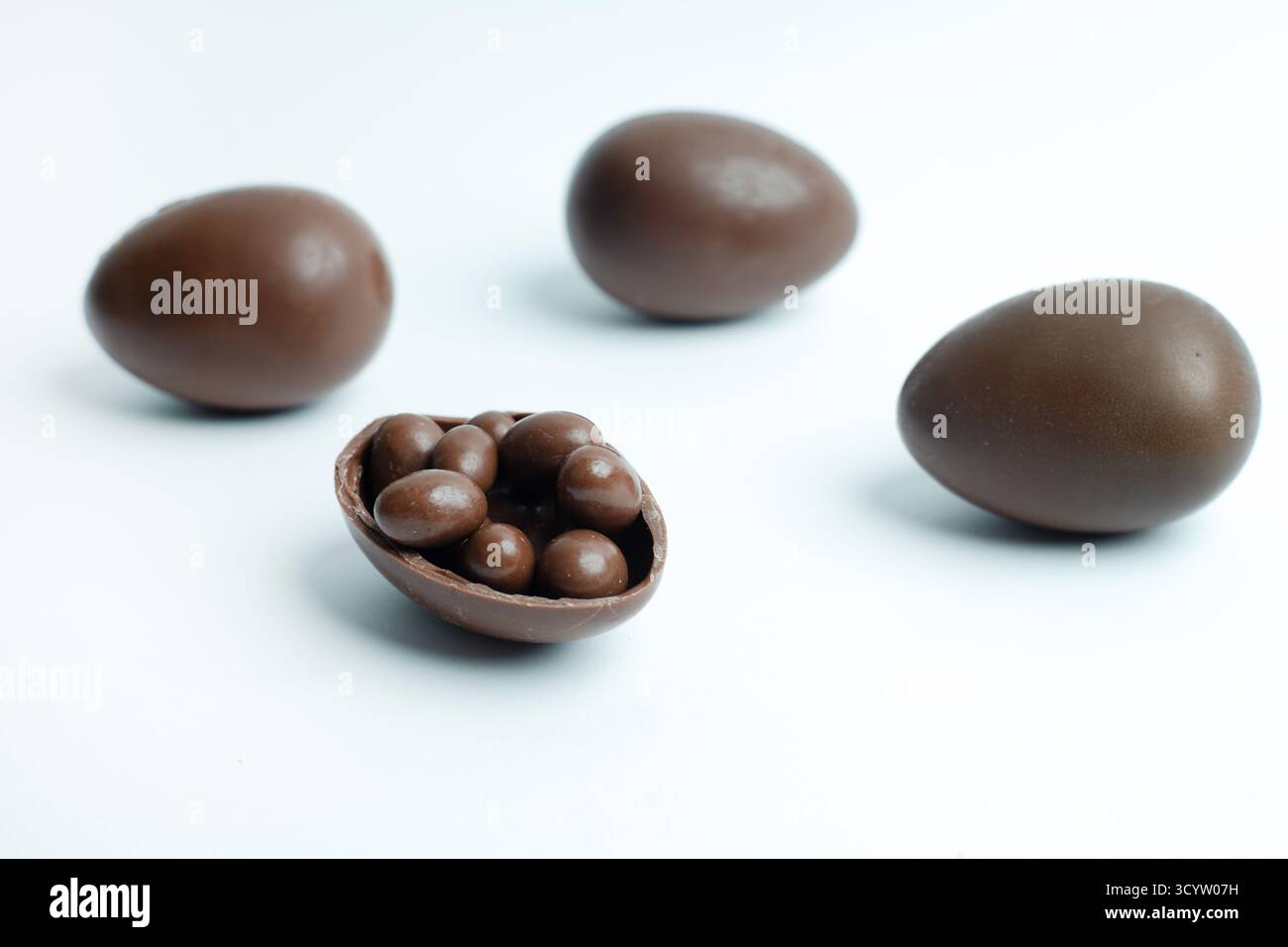 Schokoladen-Ostereier auf weißem Hintergrund, wobei eines aufgerissen ist und kleine Bonbons im Inneren enthüllt. Ein süßes Vergnügen für festliche Feiern. Stockfoto