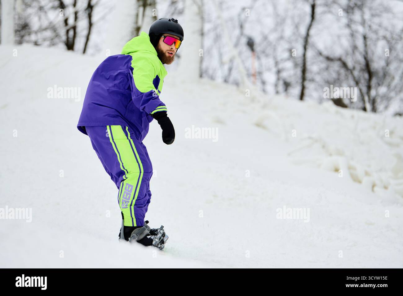 Ein Mann mit Bart rennt einen schneebedeckten Hang hinunter und zeigt seine Snowboardfähigkeiten. Stockfoto