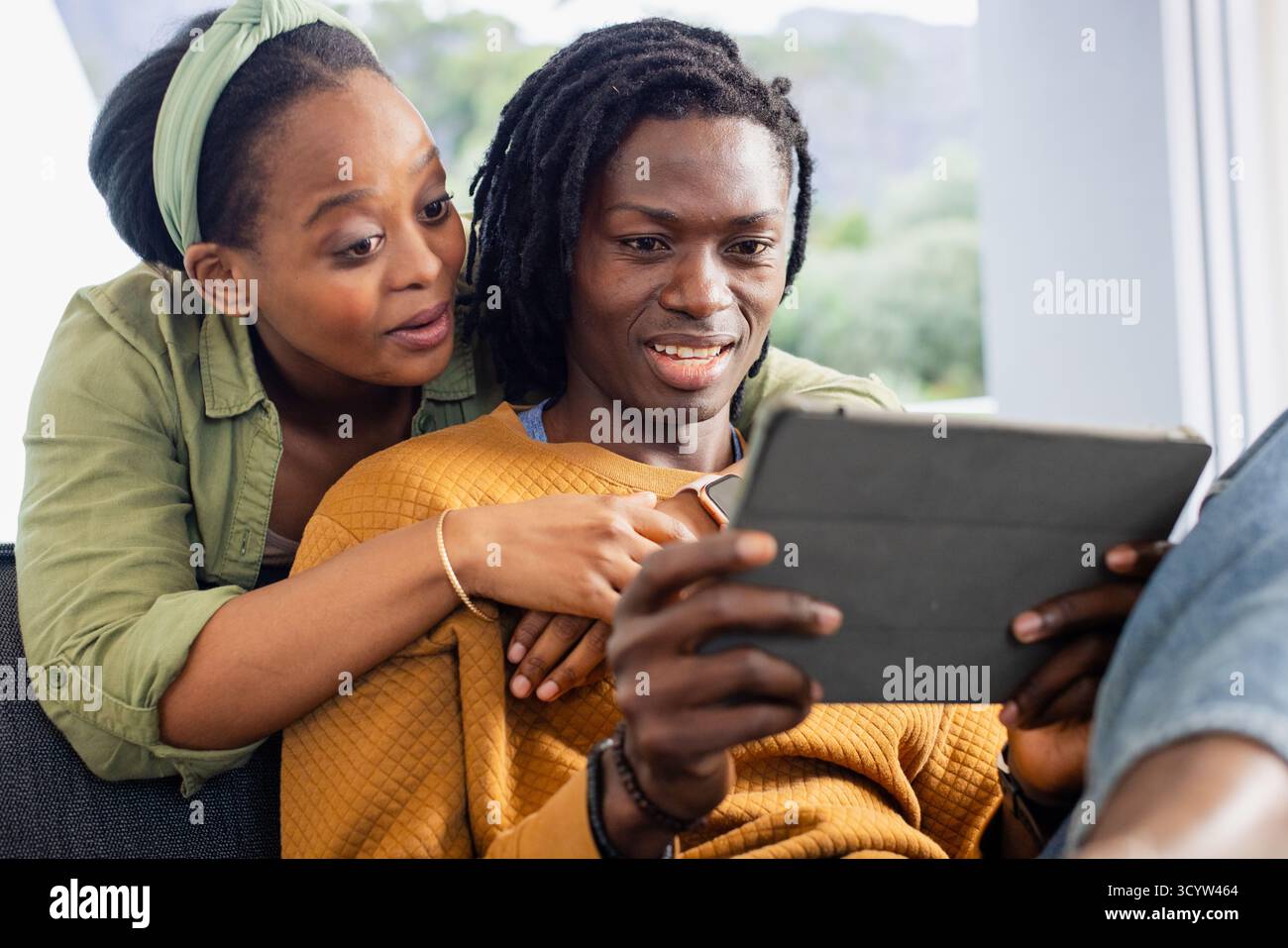 Afroamerikanisches Paar sitzt auf einem grauen Sofa im Wohnzimmer und sieht ein Tablet mit Kissen Stockfoto