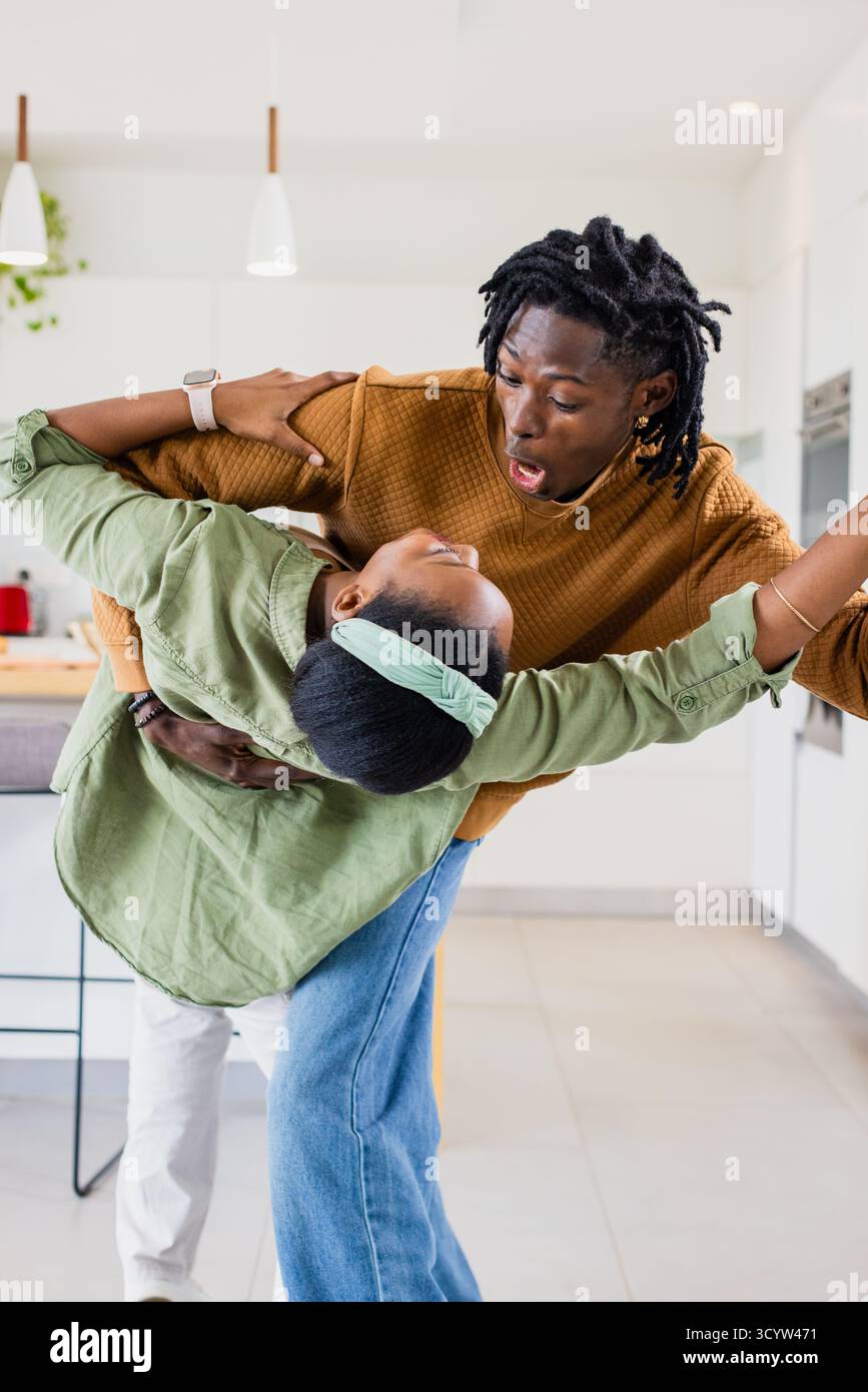 Afroamerikanischer Mann und weibliches Kind tanzt in der Küche, taucht mit Topfpflanzen auf der Insel Stockfoto