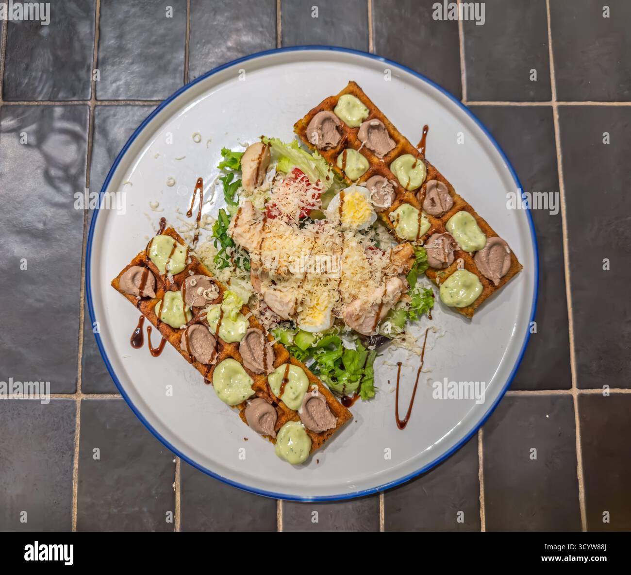 Gourmet-Caesar-Salat mit knusprigen belgischen Waffeln, Huhn, Eiern, Gurke und Balsamico-Nieseln auf weißem Teller Stockfoto