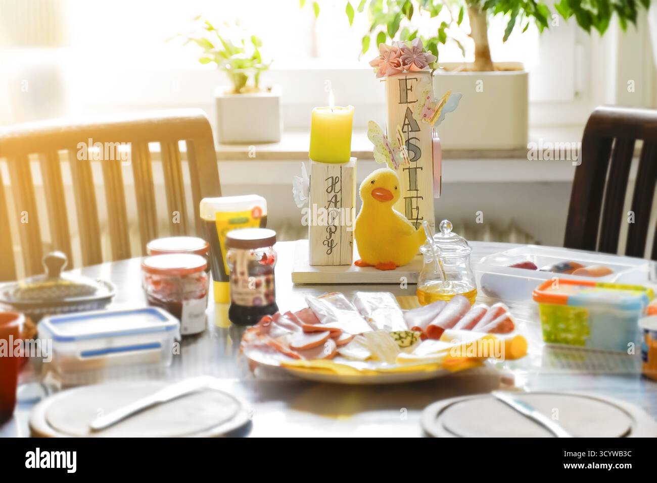 Frühstückstisch zu Hause zu Ostern. Eine Dekoration aus bemaltem Holz mit englischem Text Happy Easter dient als Kerzenhalter. Im Vordergrund befindet sich eine Platte w Stockfoto