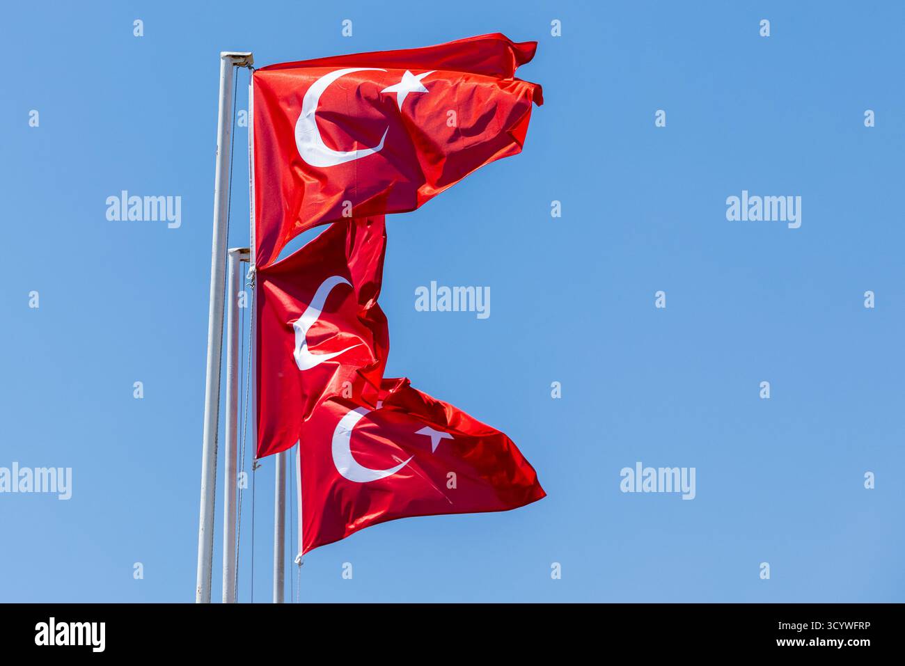 Türkische Fahnen flattern auf hohen Fahnenmasten unter einem hellblauen Himmel und fangen nationale Symbole, Bewegungen und Outdoor-Displays ein, die für eine öffentliche Veranstaltung geeignet sind Stockfoto