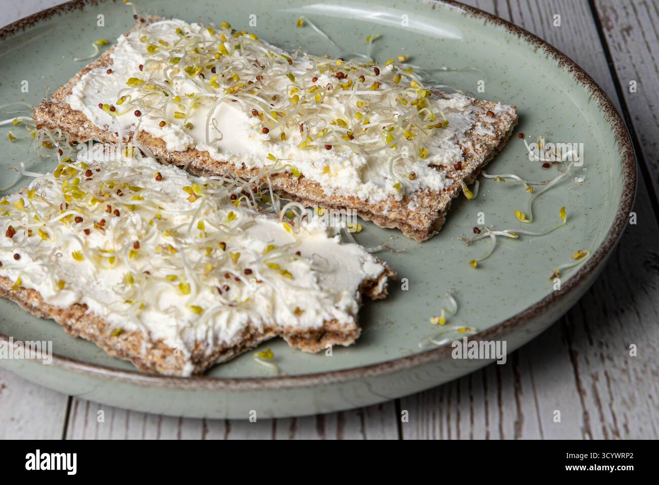 Gesundes Frühstück oder Snack mit Vollkorntoast, mit Frischkäse und Brokkoli-Sprossen, auf einem Teller, auf einem Holztisch Stockfoto