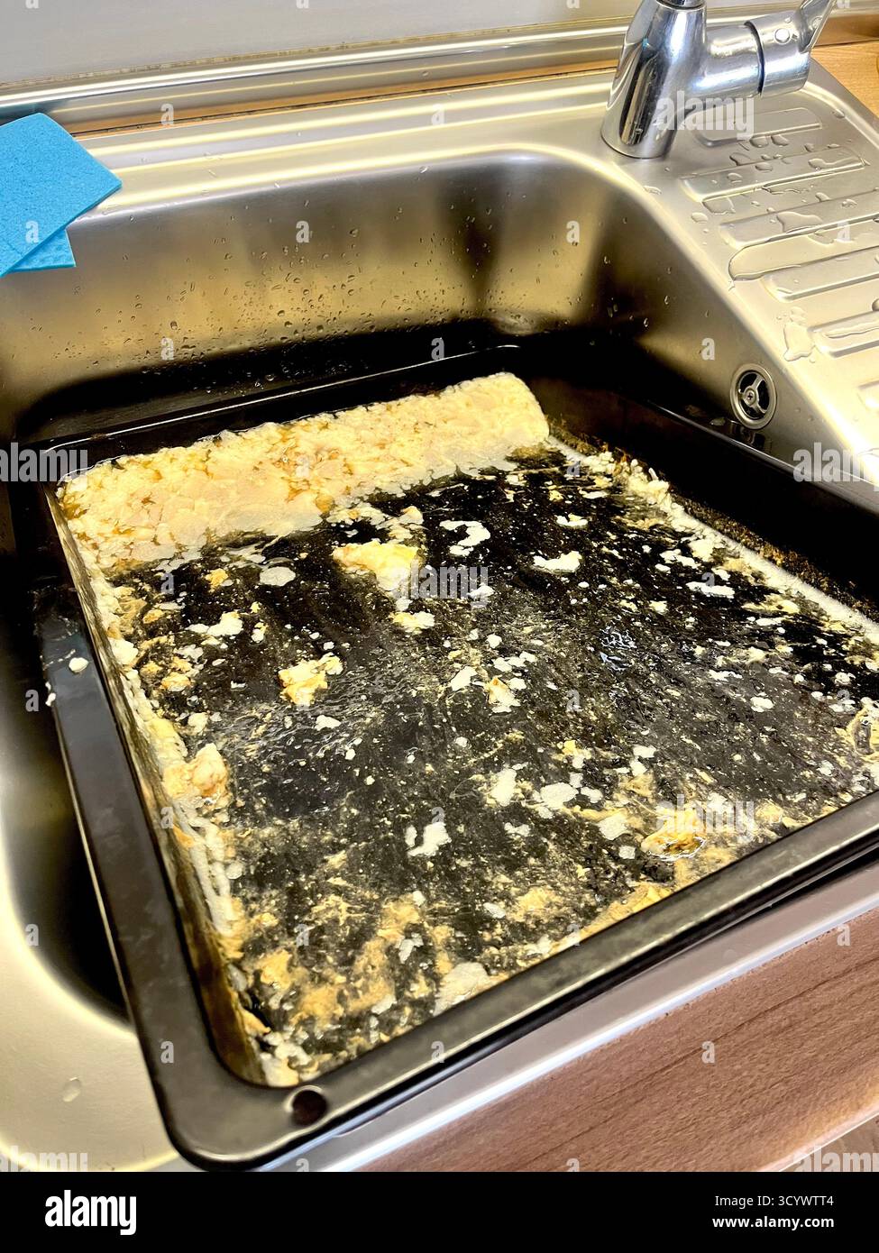 Fettgefülltes Backblech im Spülbecken nach dem Hauskochen, bereit zur Reinigung Stockfoto