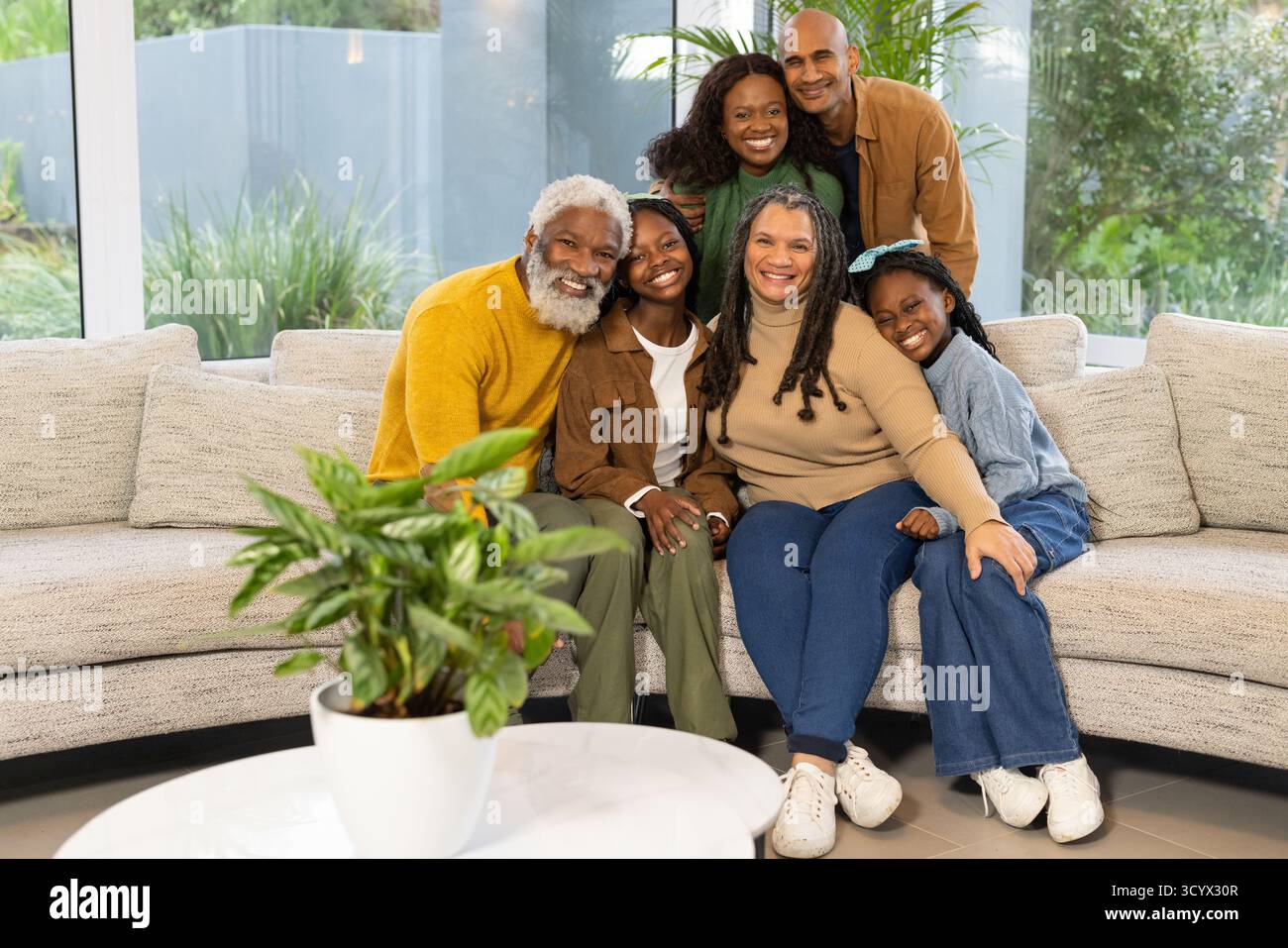 Afroamerikanische Familie trifft sich auf beigefarbenem Sofa im Wohnzimmer mit großen Fenstern Stockfoto