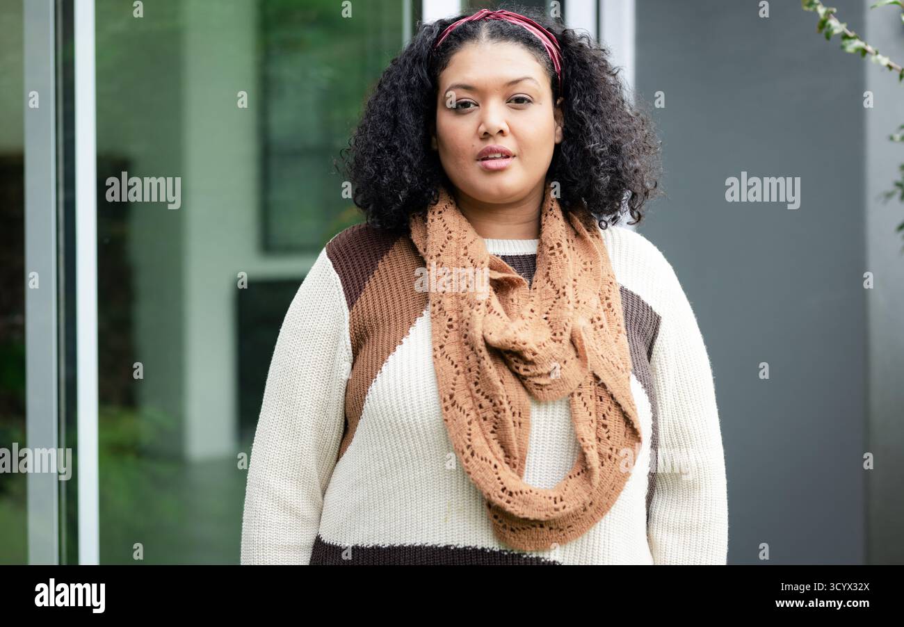 Frau stehend und trägt braunen Pullover Infinity Schal rotes Stirnband am modernen Gebäudeeingang Stockfoto