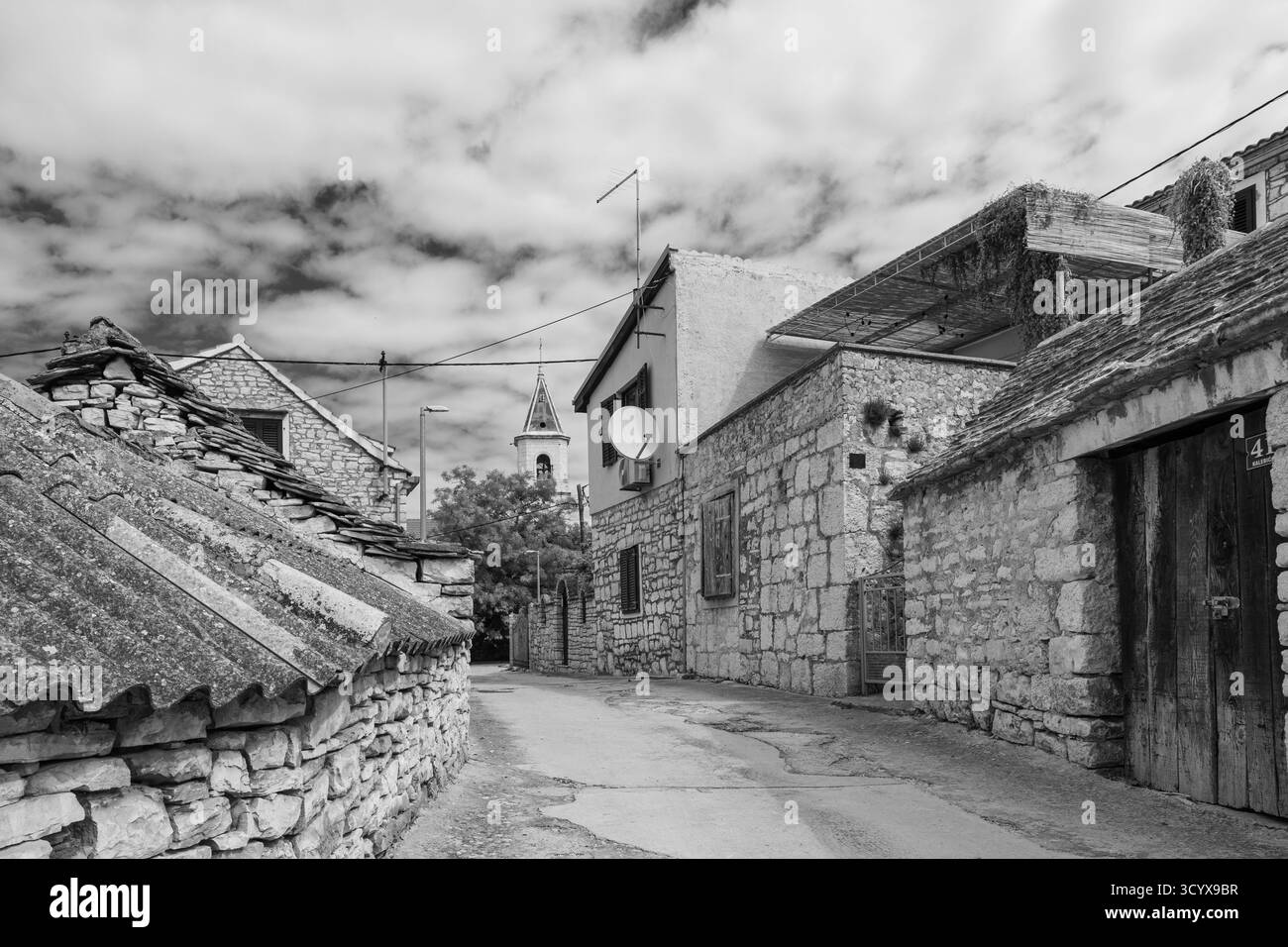 Idyllische ländliche Szene mit einem charmanten Dorf aus Stein mit einem Kirchturm umgeben von Grün unter einem leuchtend blauen Himmel. Stockfoto