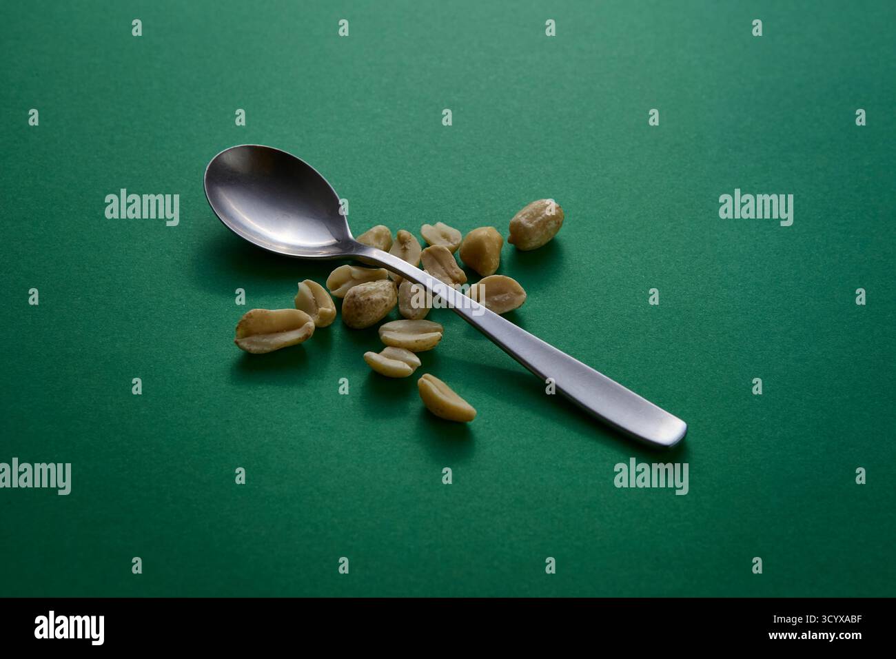 Ein silberner Löffel gefüllt mit Erdnüssen auf einem lebhaften grünen Hintergrund unter weichem Licht. Die farbenfrohe, minimalistische Einrichtung betont sauberes Essen und Natu Stockfoto