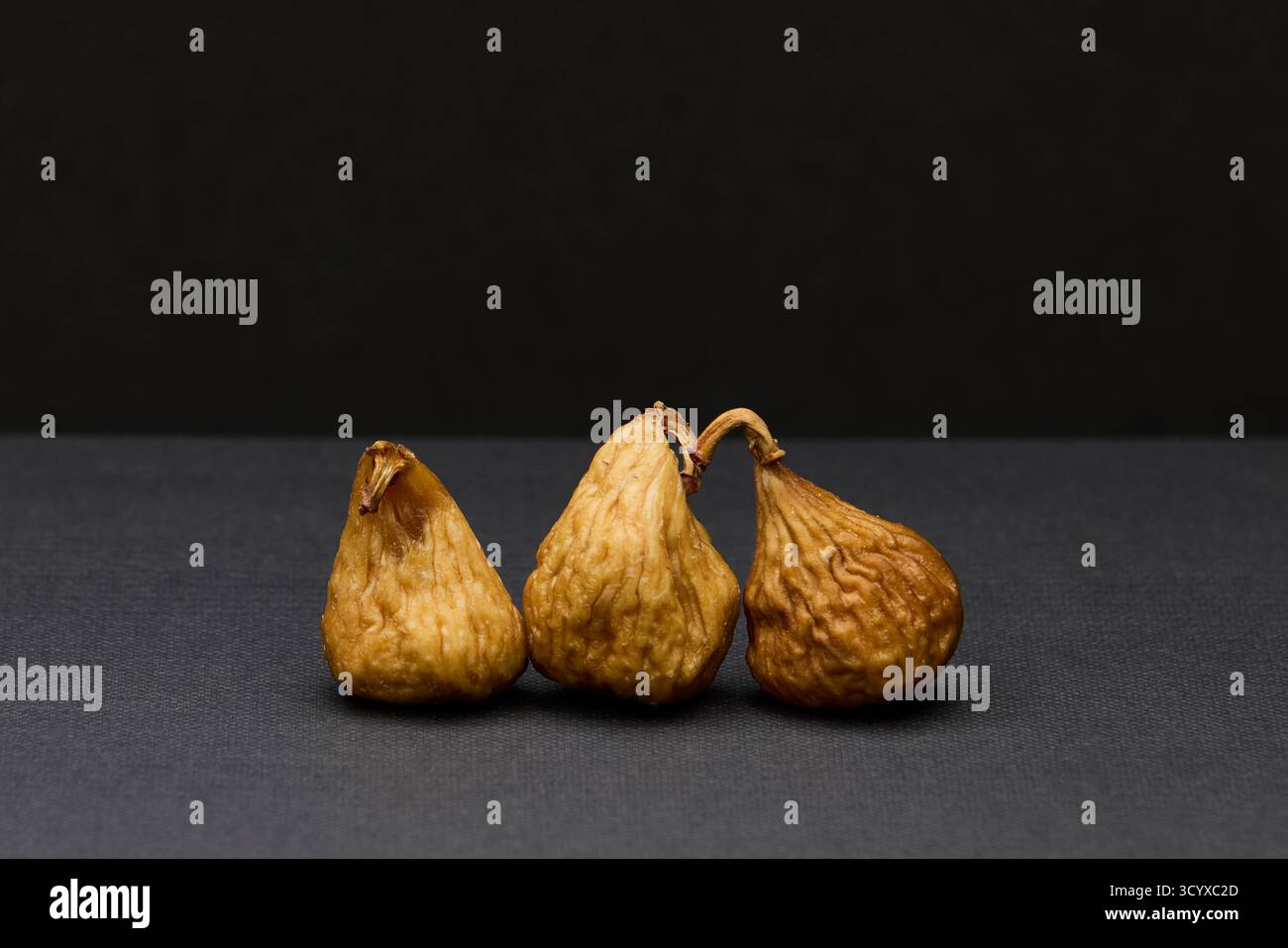 Studio Stillleben Foto von drei getrockneten Feigen auf dunkelgrauem Hintergrund. Natürliche Texturen und sanfte Beleuchtung heben organische Form und Erdton hervor Stockfoto