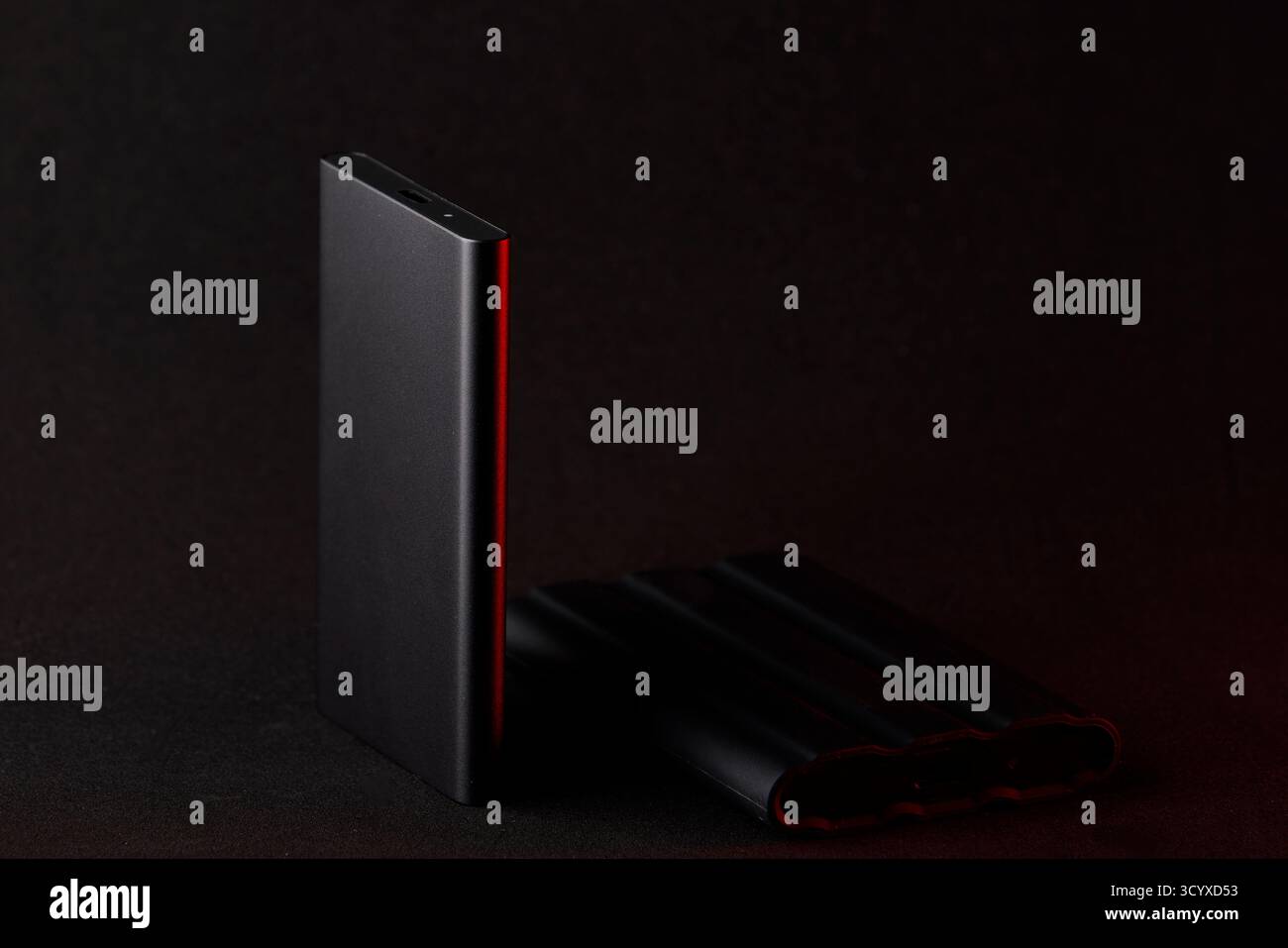 Studio-Foto eines externen SSD-Laufwerks, beleuchtet durch rote seitliche Reflexion auf dunkler Oberfläche. Minimalistisches Stillleben mit moderner Hardware Stockfoto