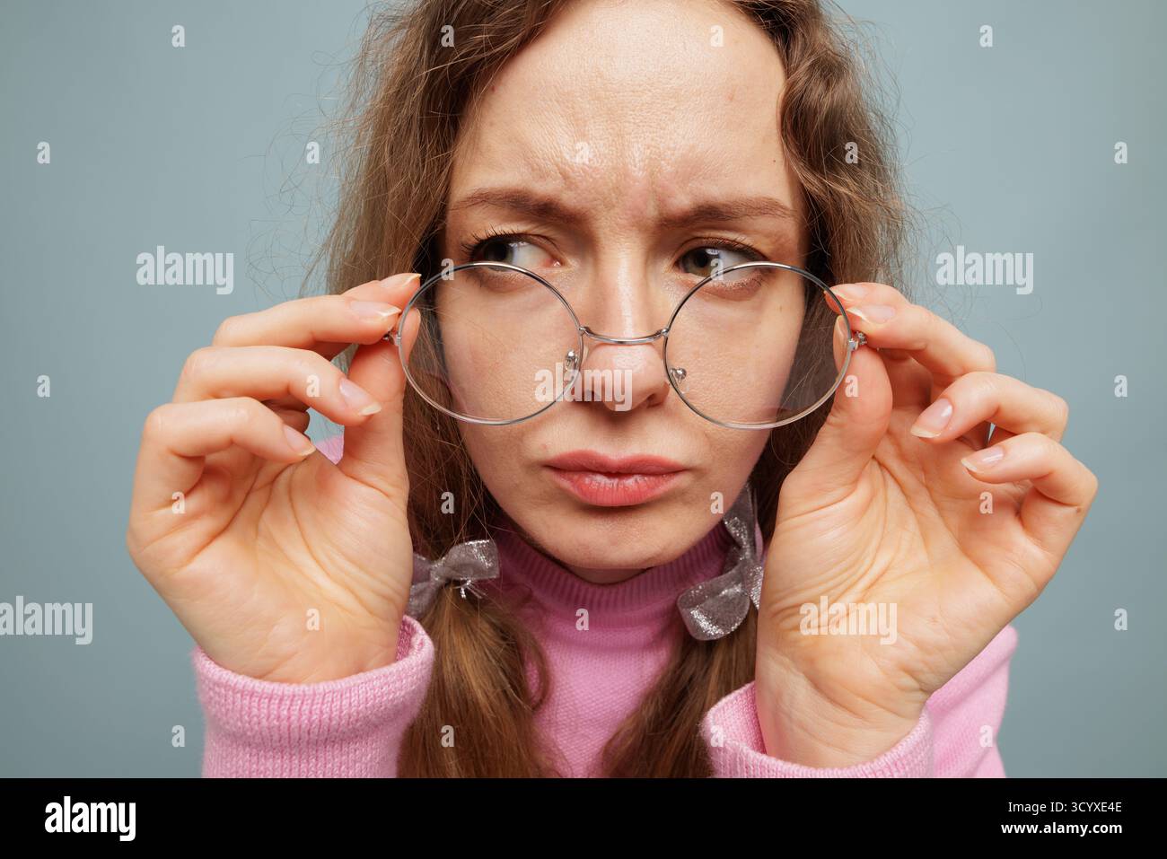 Nahaufnahme-Porträt einer Frau, die runde Brillen anpasst, mit einem skeptischen Look, der die Fokusoptometrie mit Sehschärfe und Liebe zum Detail symbolisiert Stockfoto