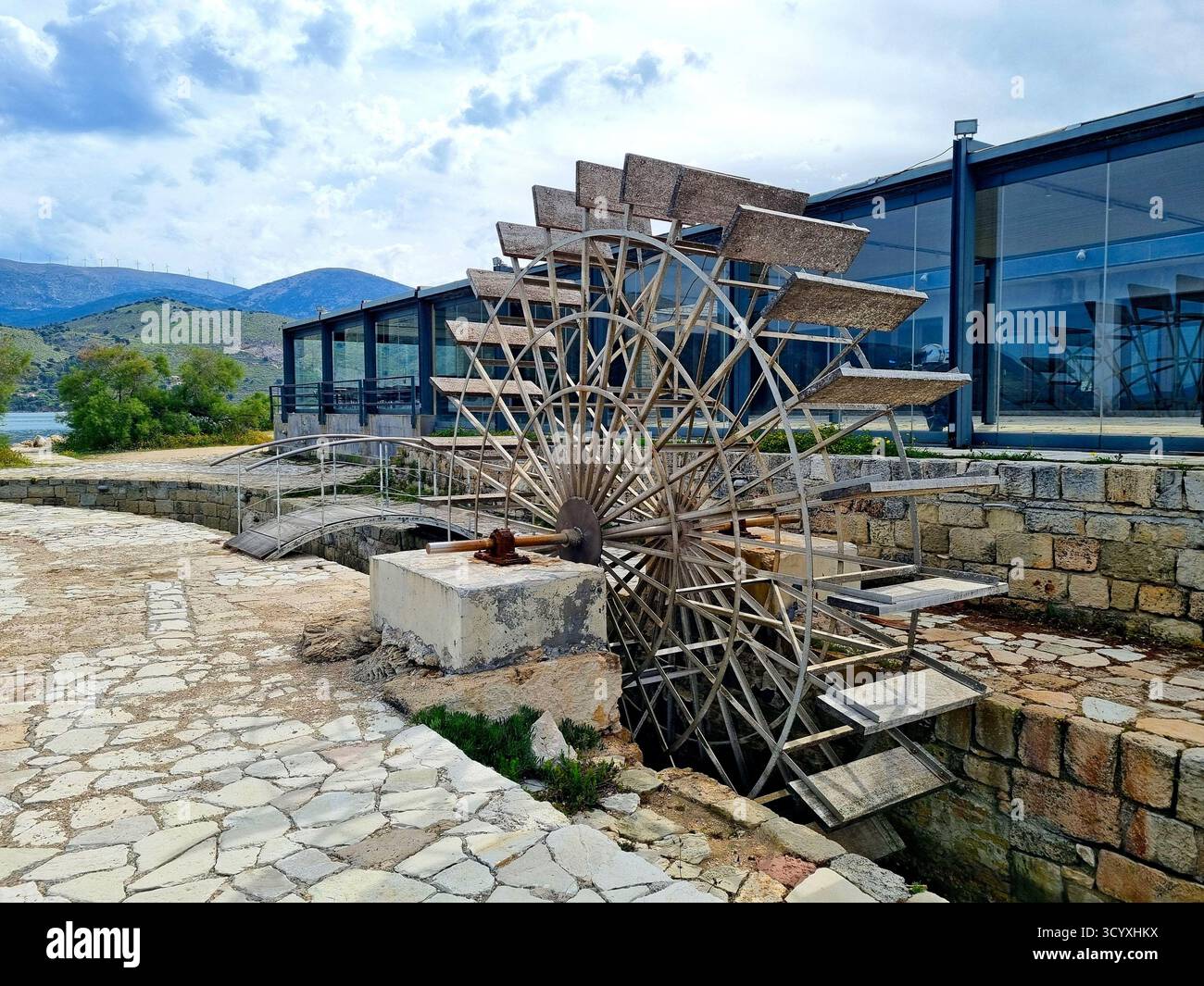 Eine alte Wassermühle vor einer Glaswand eines Restaurants in Katavothres, Argostoli, Griechenland Stockfoto