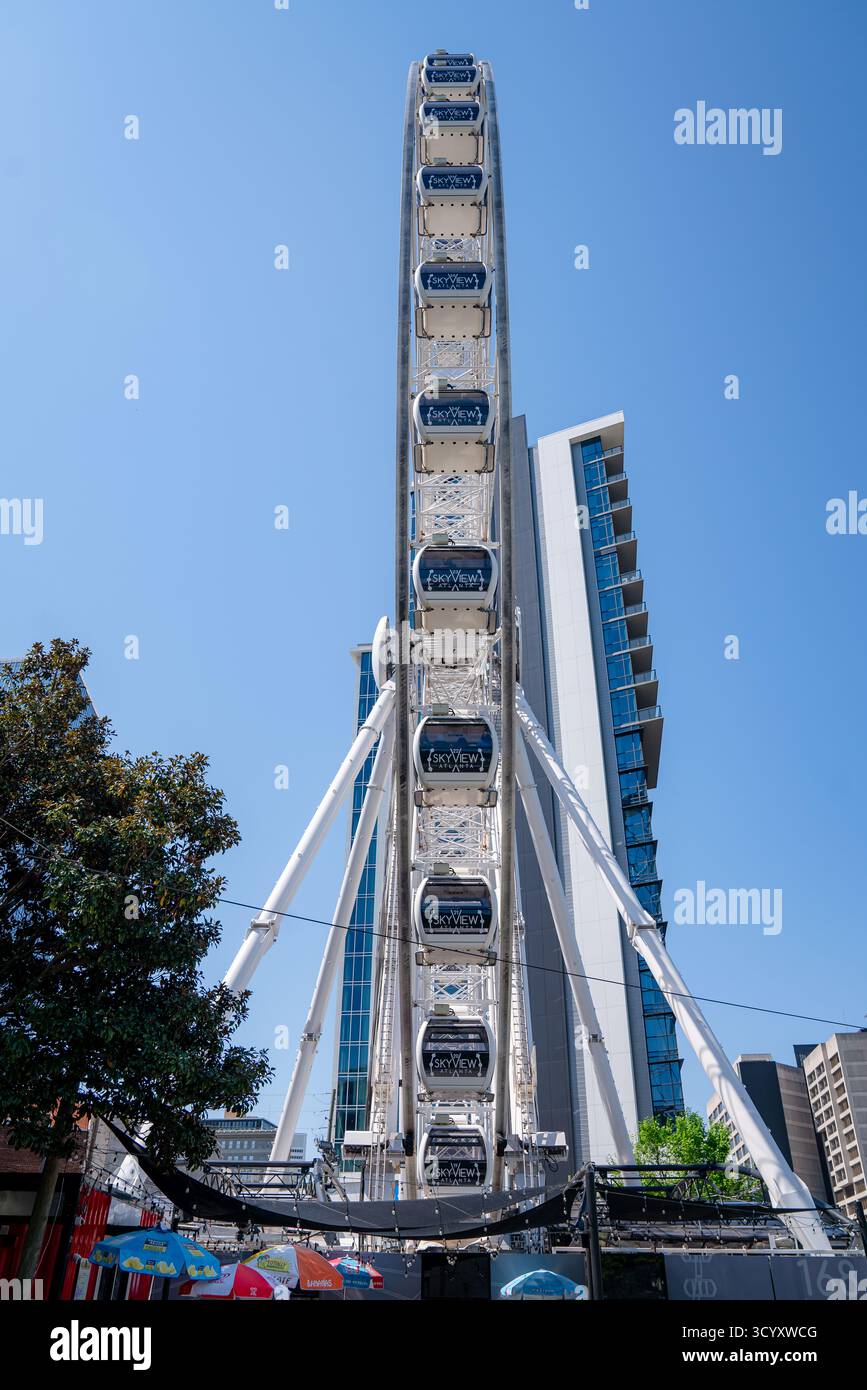 Das SkyView Atlanta Riesenrad steht hoch in der Innenstadt, eingerahmt von modernen Glasgebäuden und farbenfrohen Sonnenschirmen an einem klaren Frühlingstag Stockfoto