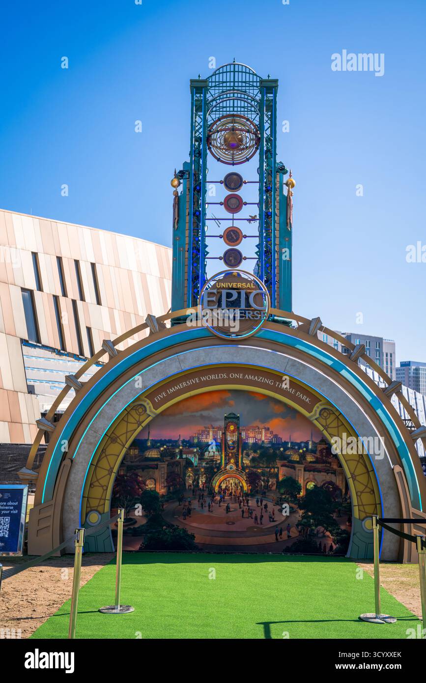 Eine Werbeausstellung für Universal's kommenden Themenpark Epic Universe steht auf einem plaza in der Innenstadt, umgeben von moderner Architektur und blauem Himmel Stockfoto
