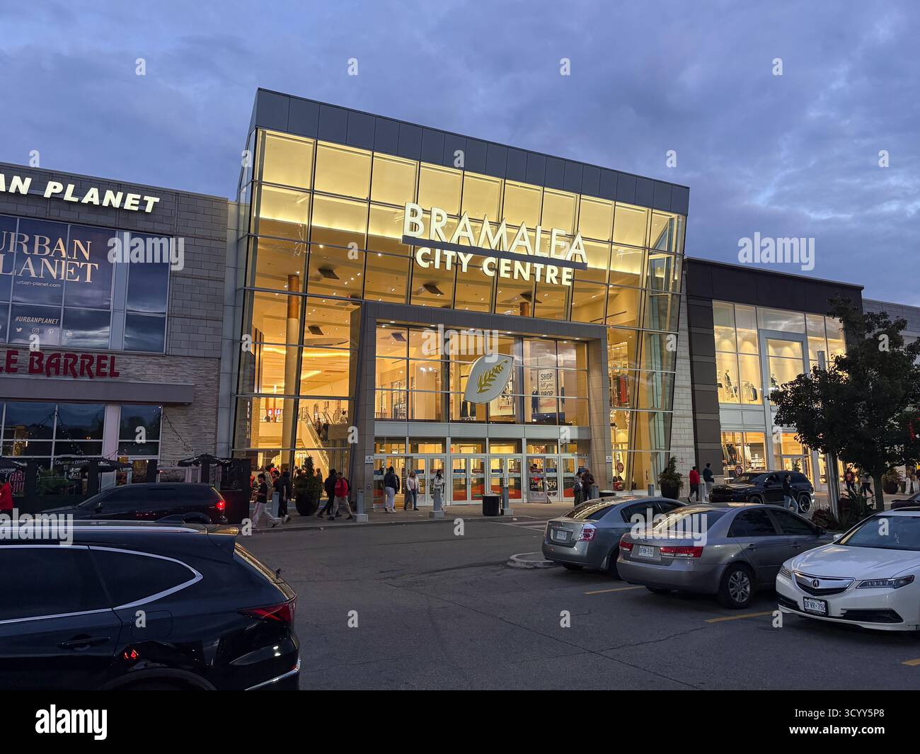 Stadtzentrum Von Bramalea. Außenansicht des Eingangs des Einkaufszentrums in der Abenddämmerung, mit geparkten Autos und Menschen sichtbar. Das Hotel befindet sich in Brampton, Kanada, und ist ein Stockfoto