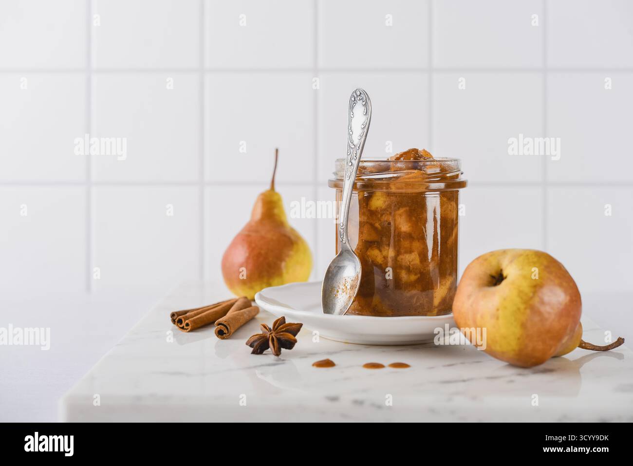 Birnenmarmelade in einem Glas mit Reifen Birnen, Zimtstangen und Teelöffel auf hellem Hintergrund Stockfoto