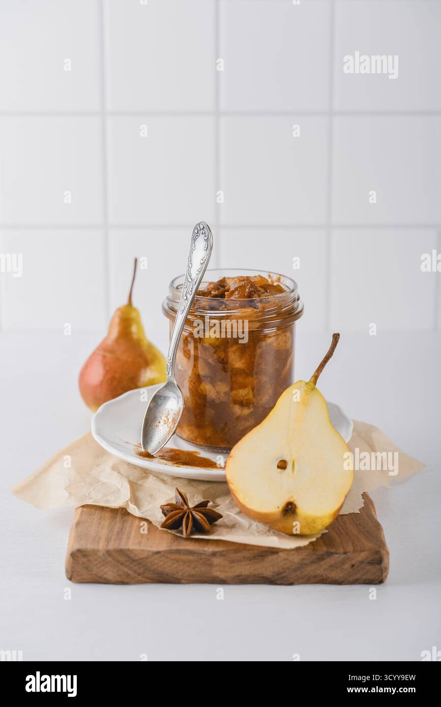 Birnenmarmelade in einem Glas mit Reifen Birnen, Zimtstangen und Teelöffel auf hellem Hintergrund Stockfoto