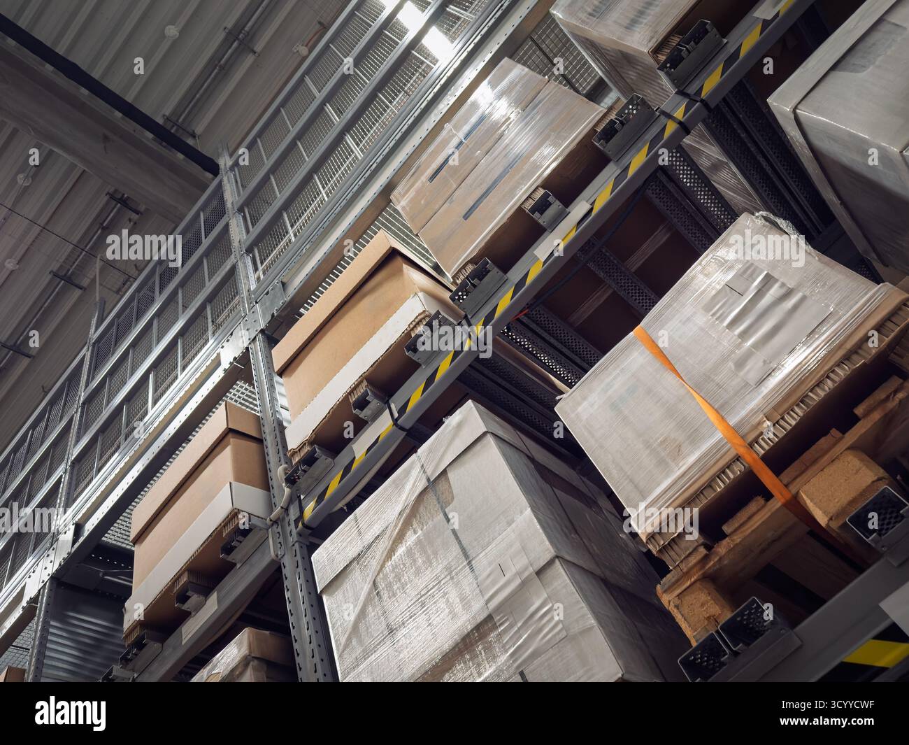 Paletten mit Kartonagen und umwickelten Waren stapeln sich auf hohen Industrieregeln in einem Lager, auf Logistikabläufen, Lagerhaltung, Versand Stockfoto