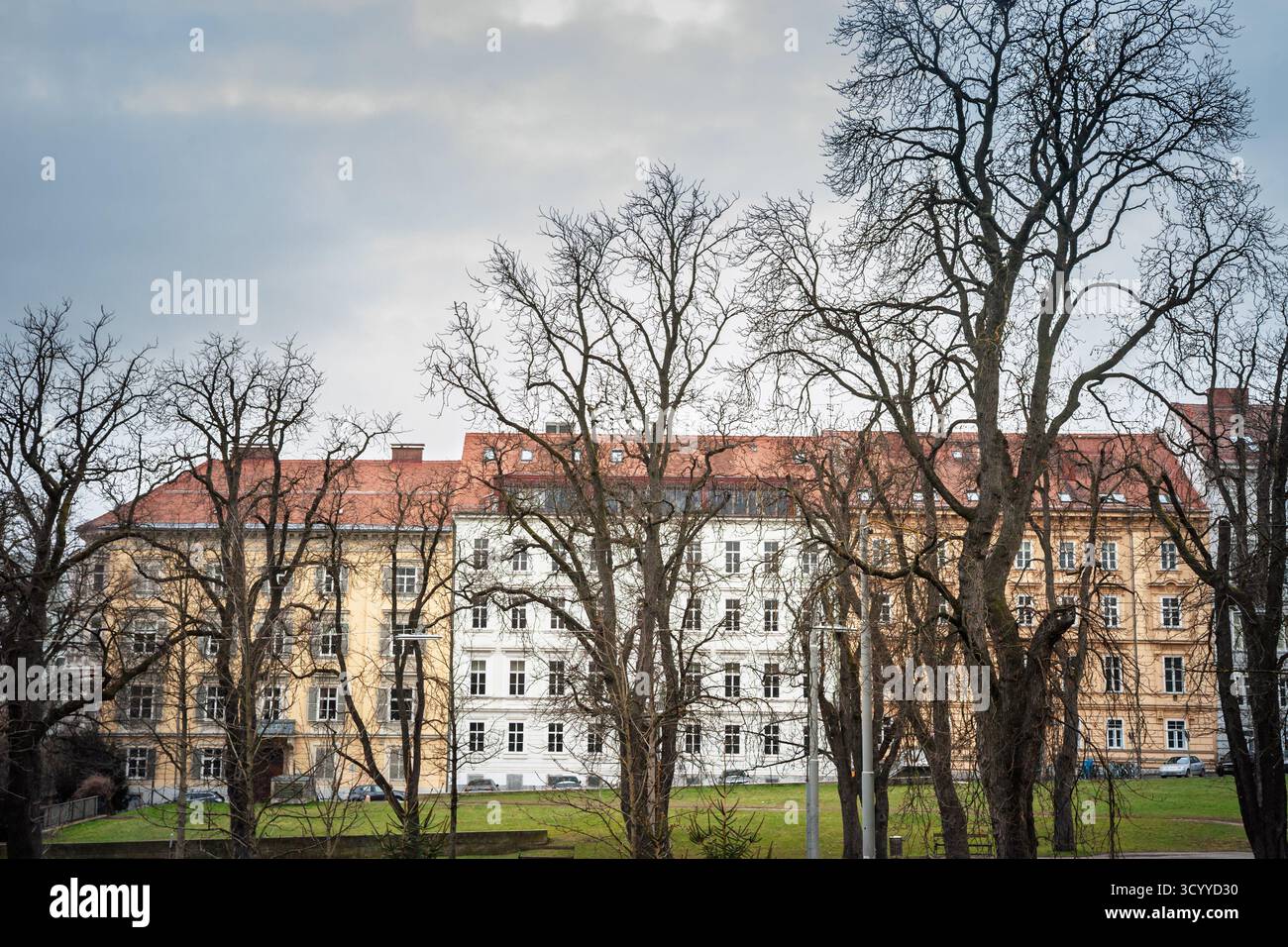 Wohnfassaden mit Blick auf einen Grazer Park mit blattlosen Bäumen, klassischer Architektur und roten Dächern, die Wohnumgebung und Grünfläche darstellen Stockfoto