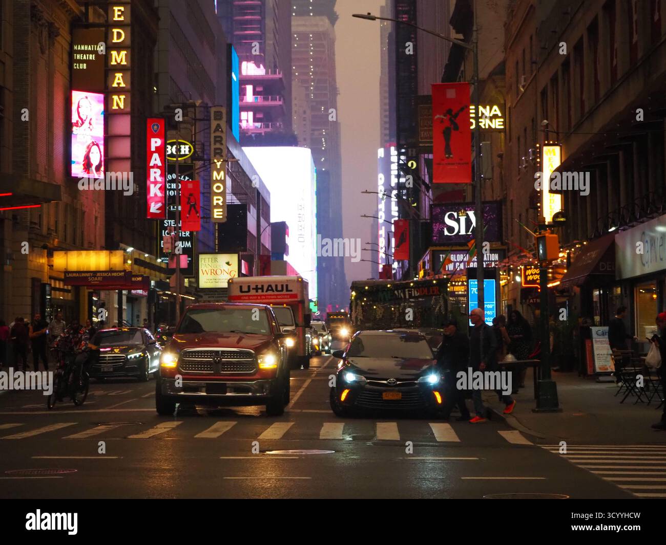 Broadway Street in der Abenddämmerung voller leuchtender Theaterschilder und Autos unter verrauchtem Himmel in New York City während des kanadischen Waldfeuers Stockfoto