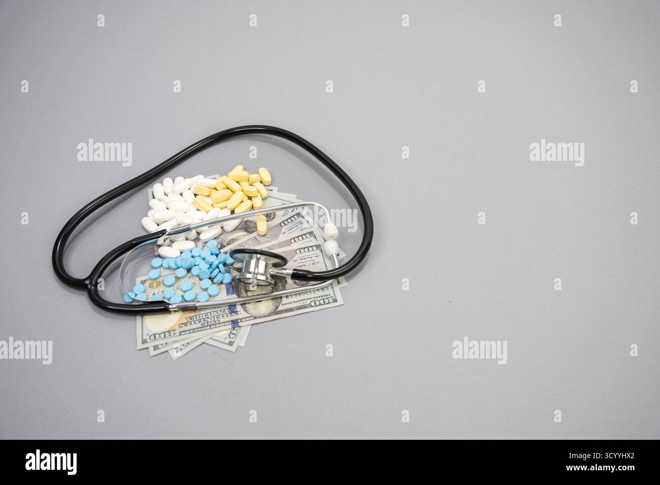 Ein Stethoskop und drei verschreibungspflichtige Tabletten auf einem Stapel von 100-Dollar-Scheinen. Stockfoto