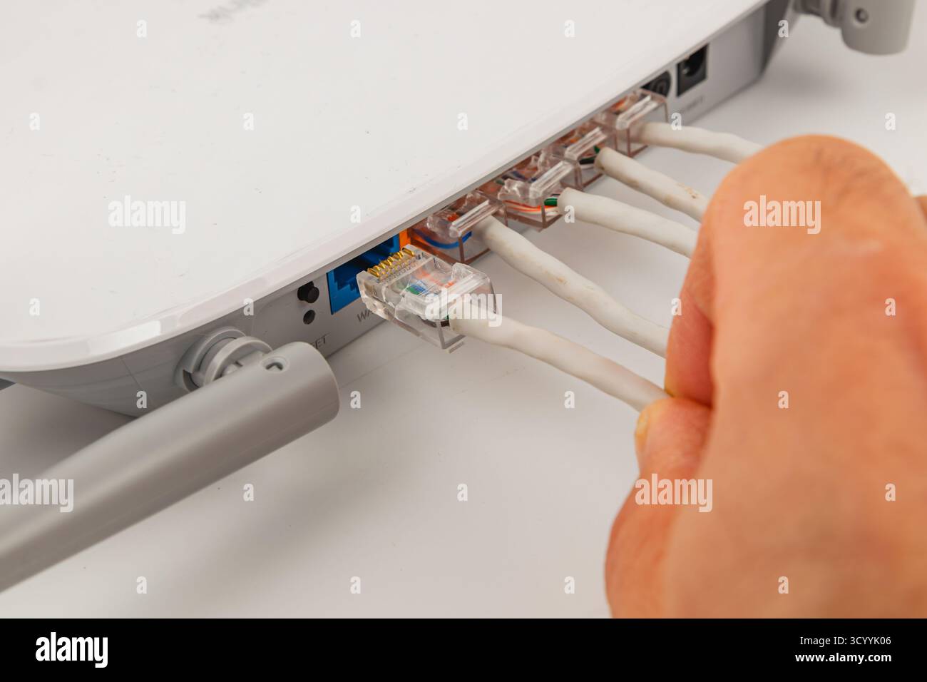 Eine Person verbindet mehrere Netzwerkkabel mit einem Router an einem Arbeitsplatz. Diese Konfiguration ist für den Internetzugang und die Effizienz des Heimnetzwerks von entscheidender Bedeutung. Stockfoto