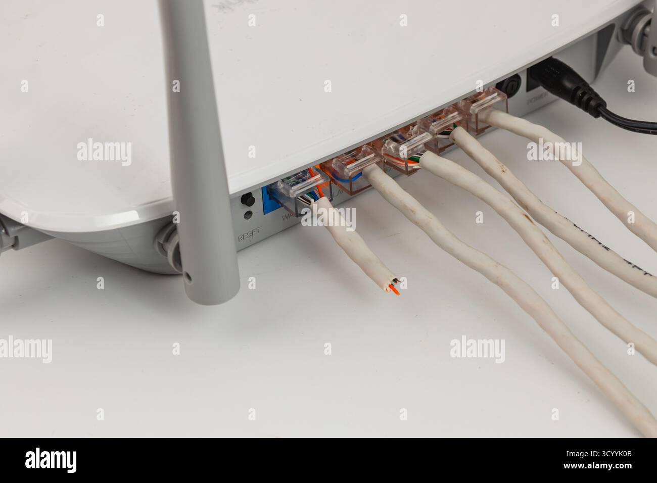 Ein Netzwerkgerät wird auf einem Schreibtisch mit mehreren Kabeln auf der Rückseite platziert. Die Einstellung zeigt die Kabel an, die für einen organisierten Arbeitsbereich ordentlich angeordnet sind Stockfoto