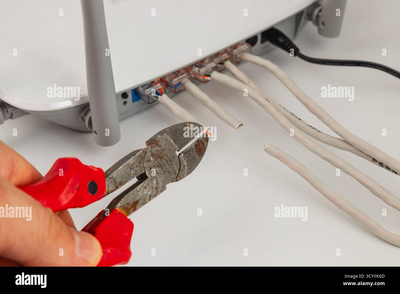 Eine Person verwendet Drahtschneider, um ethernet-Kabel zu schneiden, die mit einem Router in einem Heimbüro verbunden sind. Diese Aktivität ist für die Schaffung eines zuverlässigen Systems von entscheidender Bedeutung Stockfoto