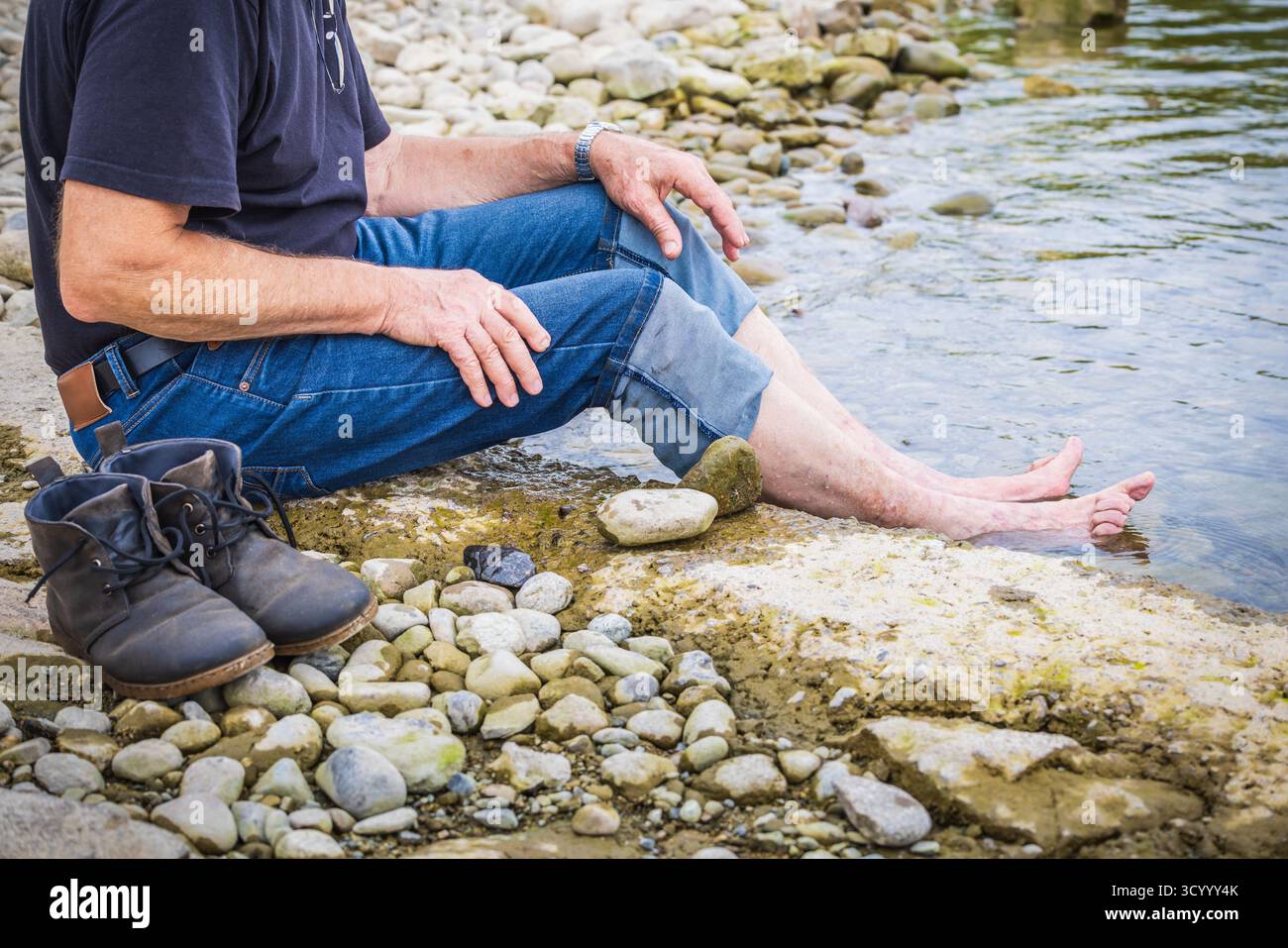 Ein älterer Mann kocht müde und geschwollene Füße in einem natürlichen Fluss oder See und entspannt sich Stockfoto