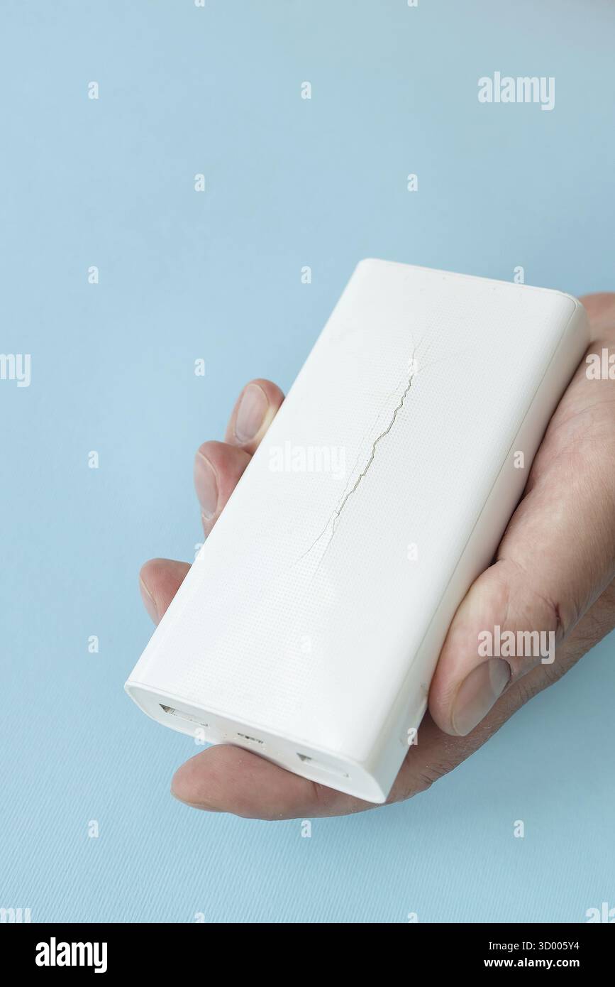 Powerbank in der Hand, eine Batterie, die unbrauchbar geworden ist, sich ausdehnt und ausdehnt, bis das Gehäuse bricht. Es besteht Explosionsgefahr Stockfoto