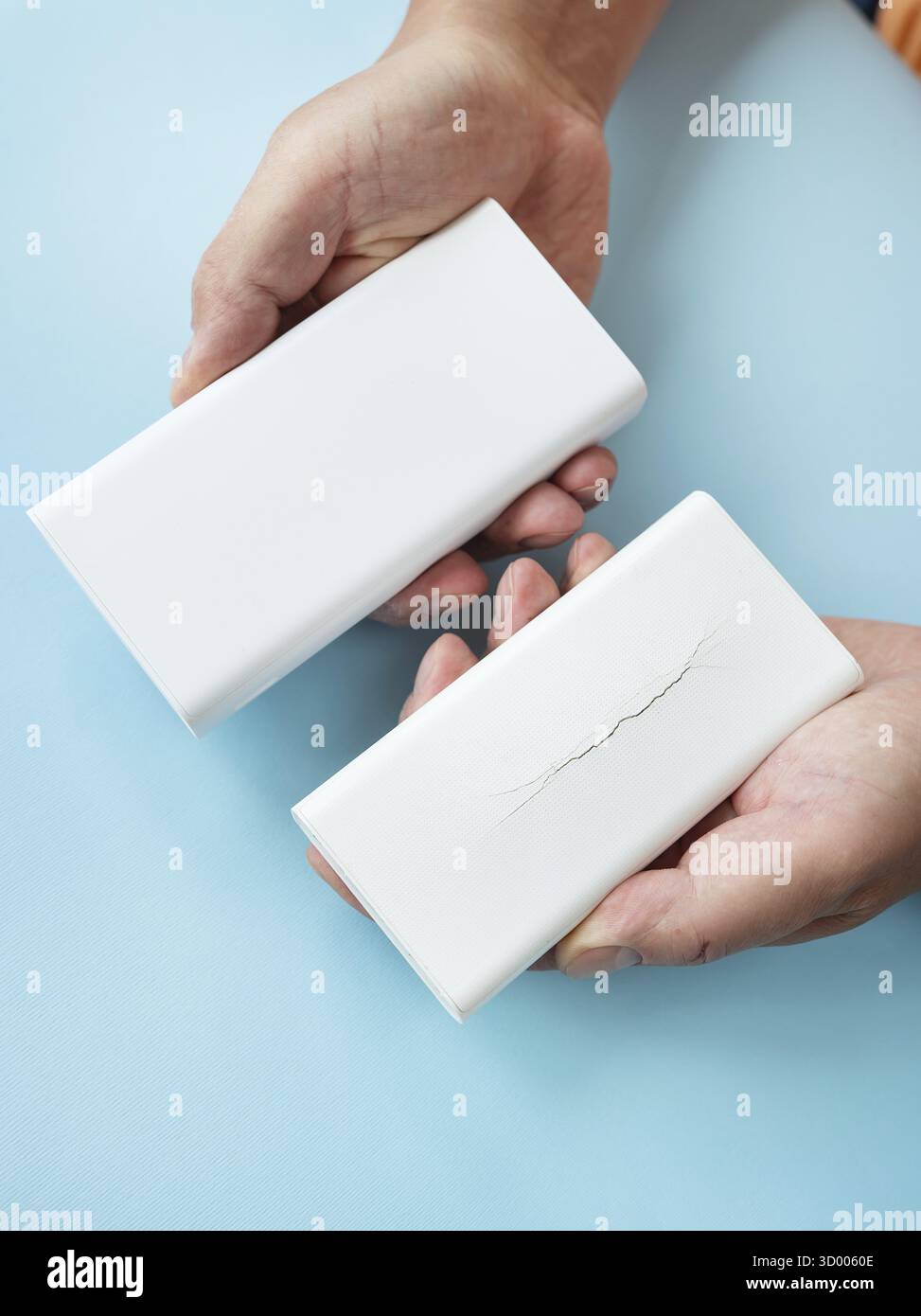 Hände, die eine neue und eine gebrochene Powerbank auf blauem Hintergrund vergleichen Stockfoto