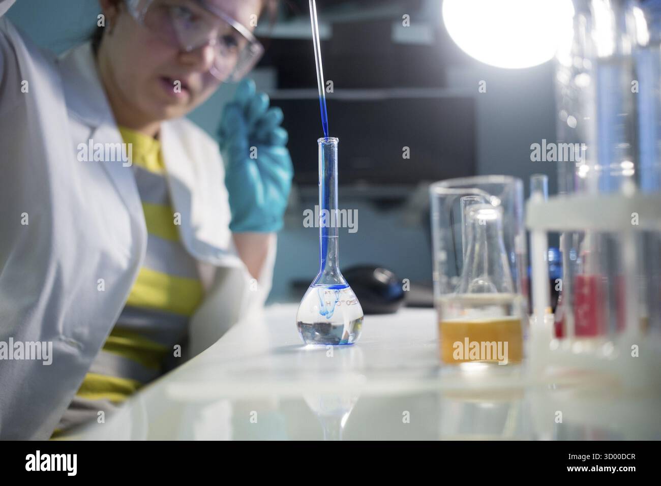 Labortechniker in Schutzbrille und Labormantel mit Kolben im Chemielabor Stockfoto