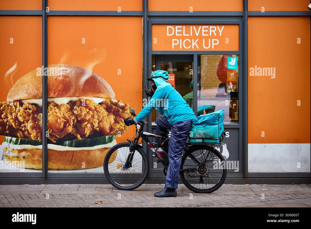 Deliveroo Radfahrer bei Manchester Piccadilly Lieferfenster für die Abholung eines Popeyes Stockfoto