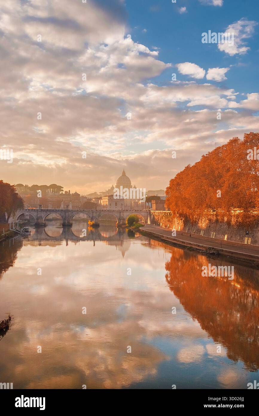 Herbst und Laub in Rom. Wunderschöne Platanen-Orangenblätter entlang des Tiber mit der berühmten Petersdom-Kuppel und der Heiligen Engel-Brücke bei Sonnenuntergang Stockfoto