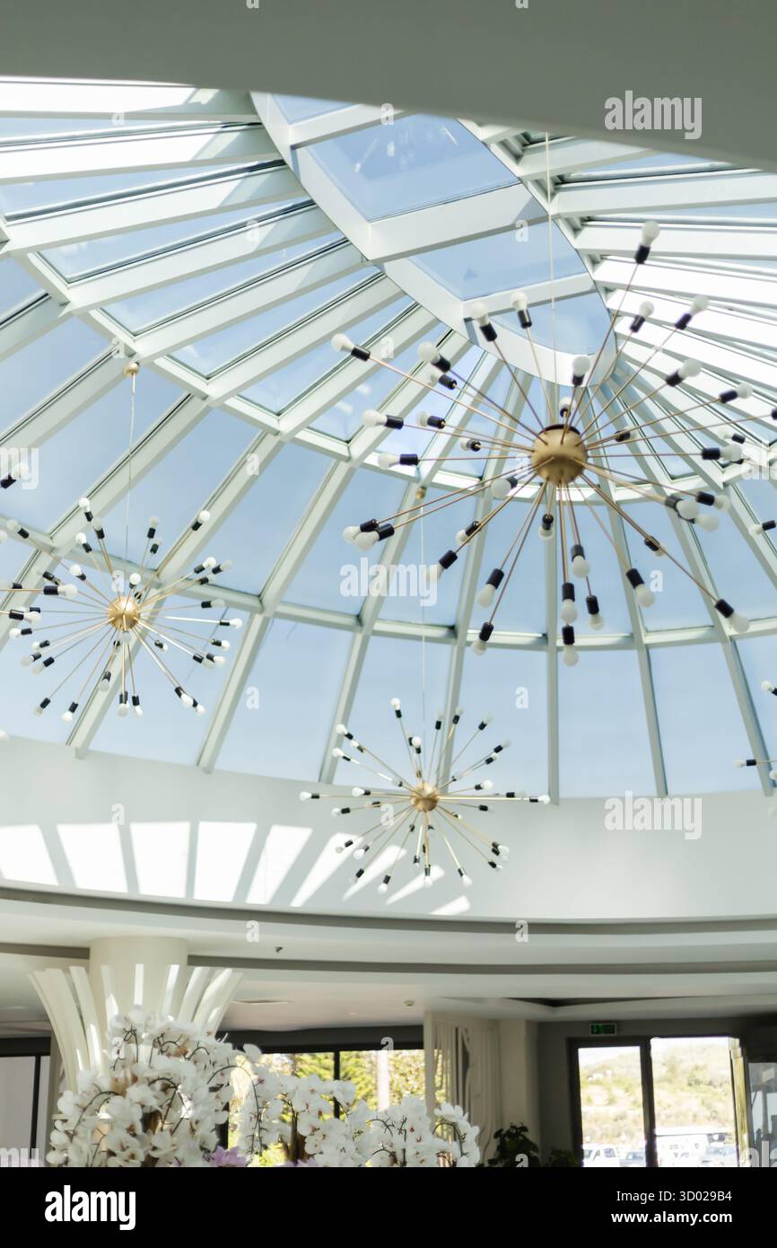 Ein geräumiger Raum verfügt über eine wunderschöne Glasdecke, in der natürliches Licht einströmen kann. Moderne Leuchten verleihen der Atmosphäre einen Hauch von Eleganz Stockfoto