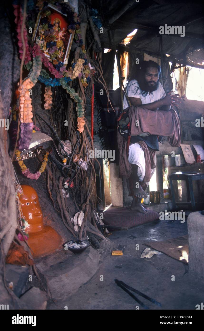 Buße ein Hinduheiliger Mann, ein Sadhu, steht auf einem Bein und ruht auf einer Schaukel. Er ist auf der zweiten Buße (im zweiten Jahr) jede Buße ist für 7 Jahre, steht nur auf einem Bein. Hanuman India God, eine hinduistische Gottheit am Fuß des Banyan Baumes. Mumbai Bombay Indien. Um die 1983 1980er Jahre HOMER SYKES Stockfoto