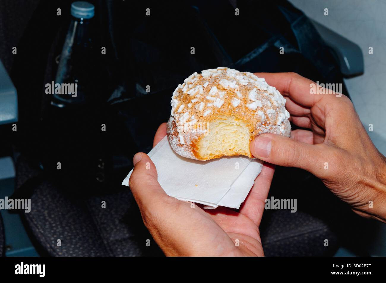 Nahaufnahme eines Mannes mit einer Brioche con granella di Zucchero, einem traditionellen italienischen Gebäck mit Zuckerkristallen, in einem Zug oder Bus während seiner Zeit Stockfoto